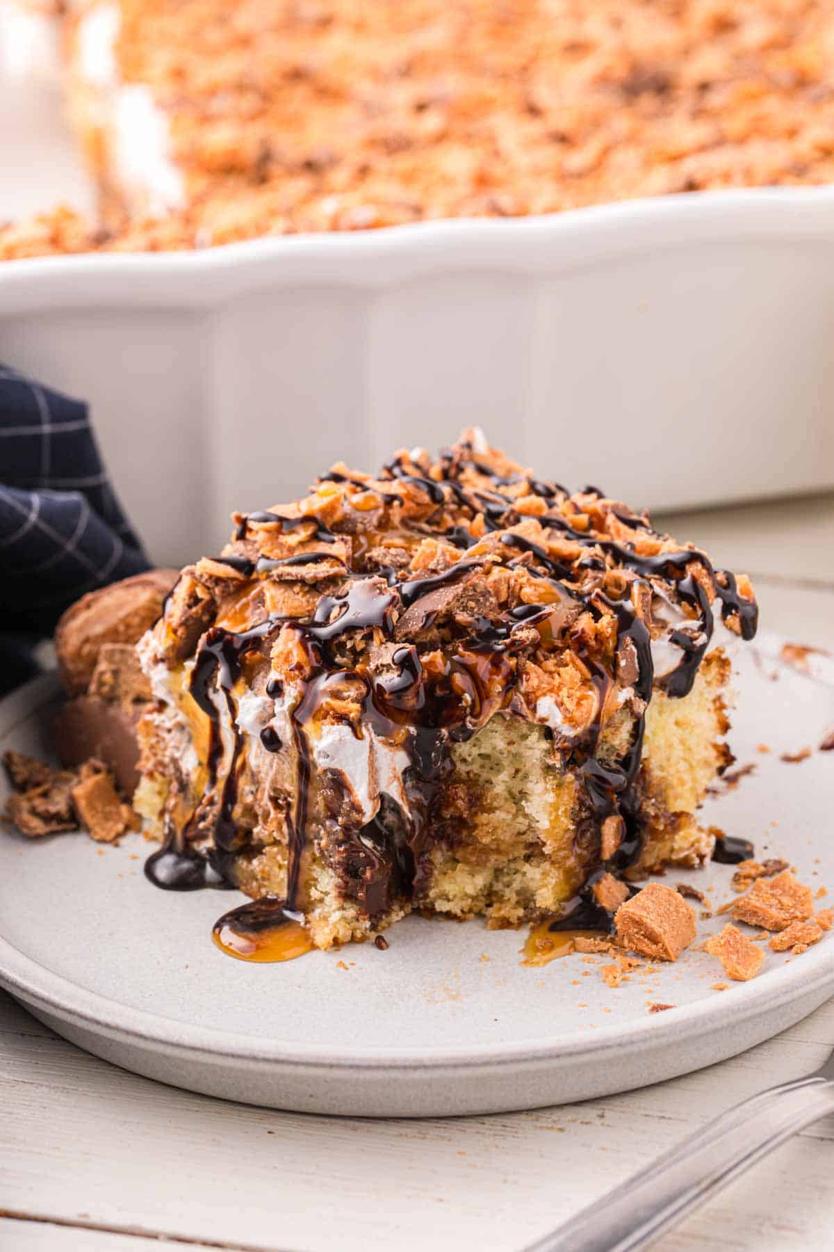 Butterfinger Poke Cake is a decadent dessert starting with a golden cake filled with chocolate and caramel sauce and topped with whipped topping and chopped Butterfinger chocolate bars.