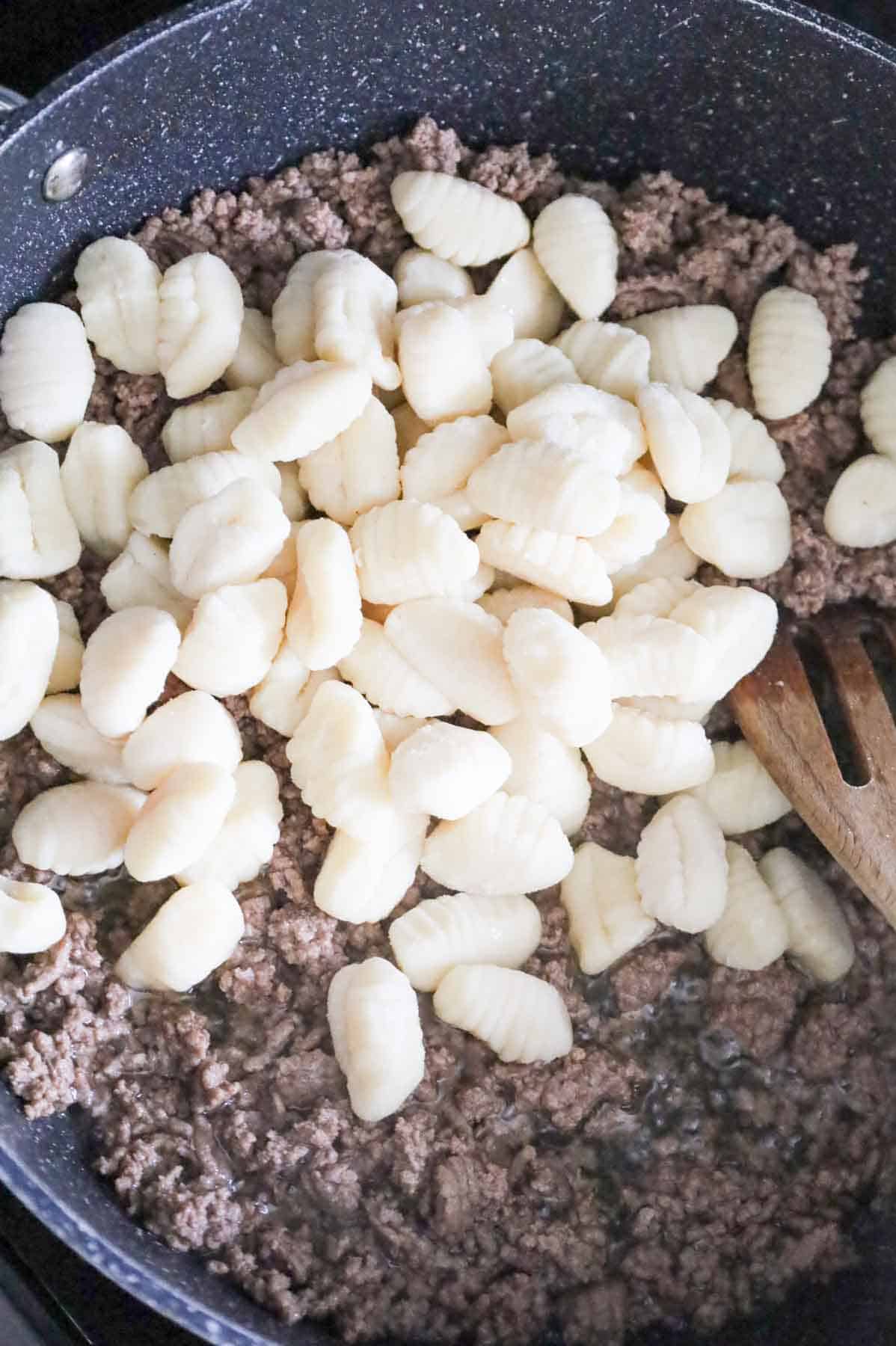 potato gnocchi on top of cooked ground beef in a skillet