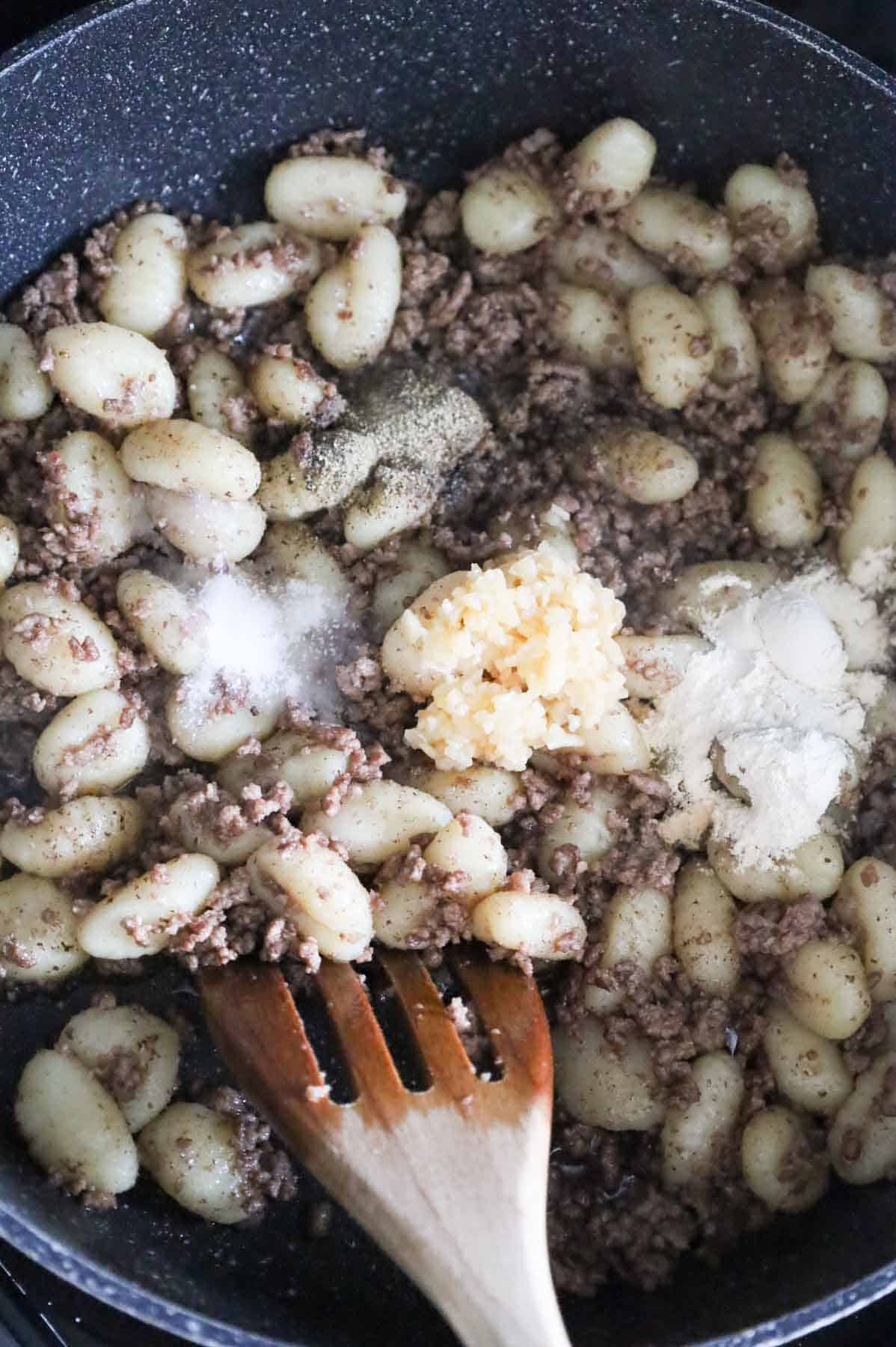 minced garlic, salt, pepper and onion powder on top of ground beef and gnocchi in a skillet