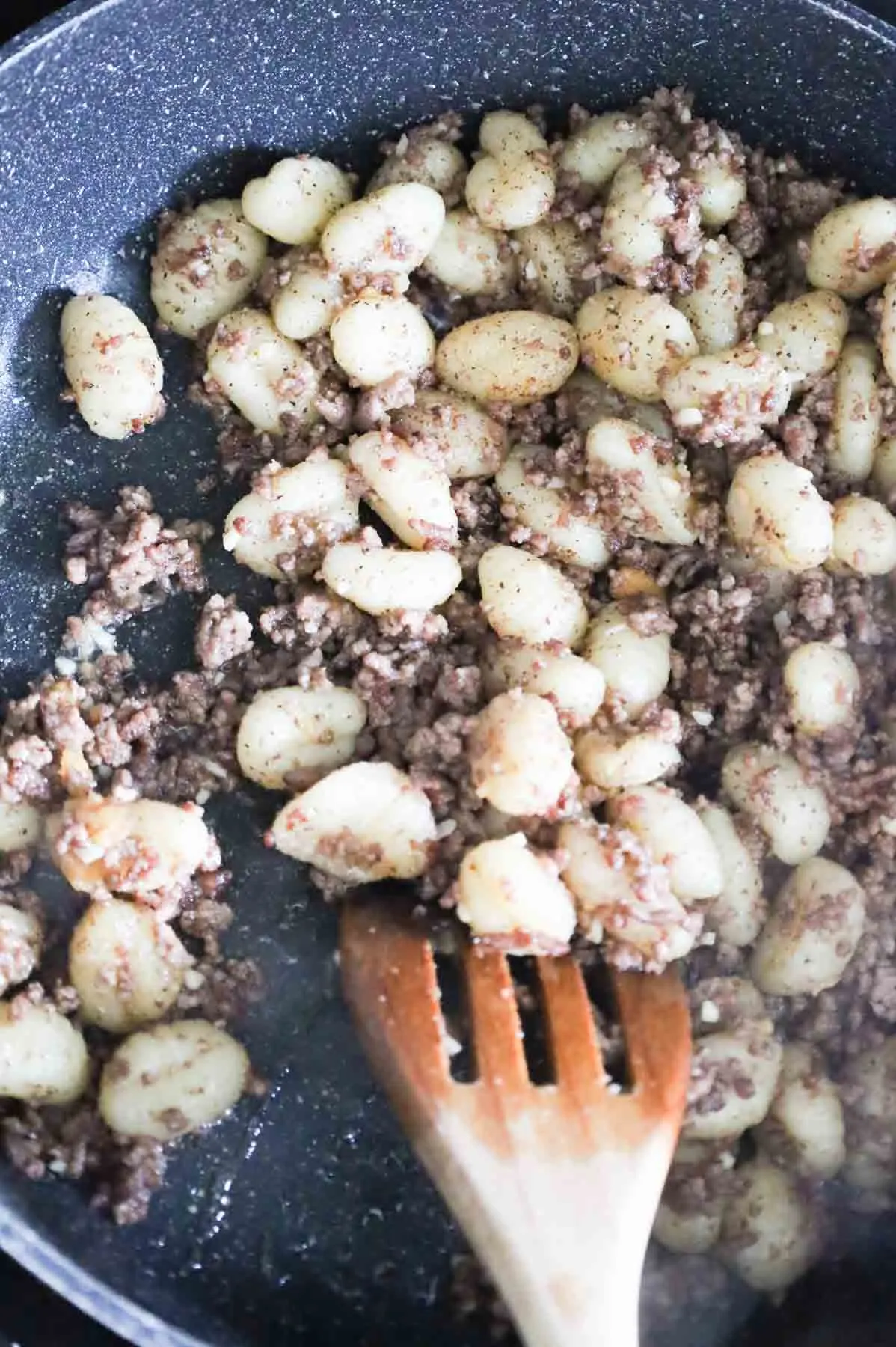 ground beef and gnocchi being stirred in a skillet while cooking
