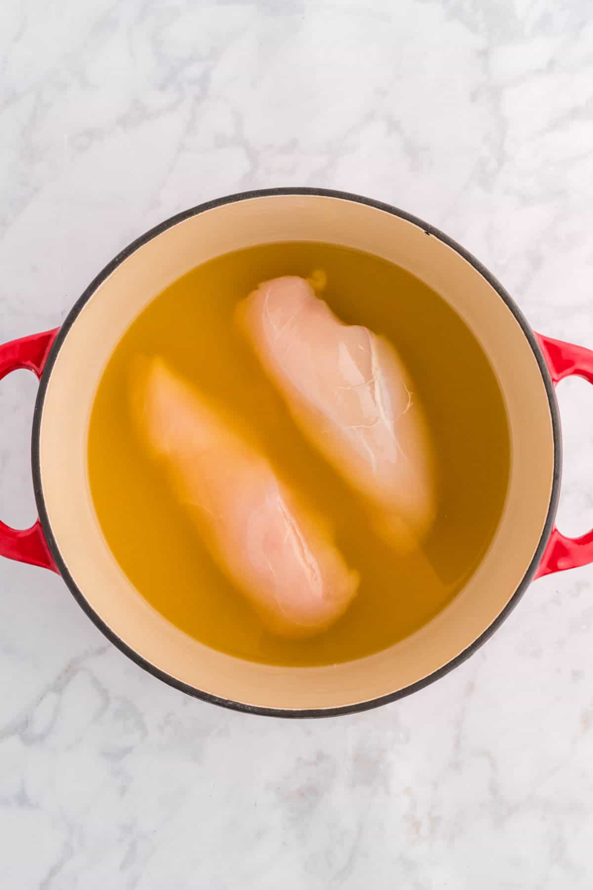 raw chicken breasts in broth in a large pot