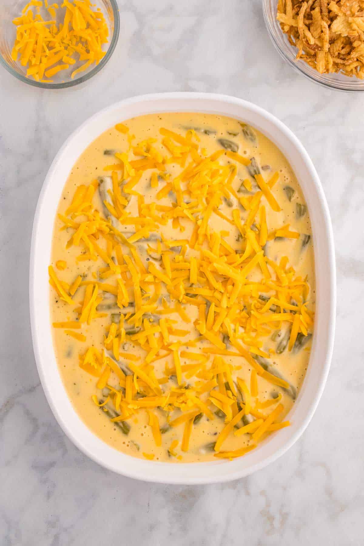shredded cheddar cheese on top of creamy velveeta and green bean mixture in a casserole dish