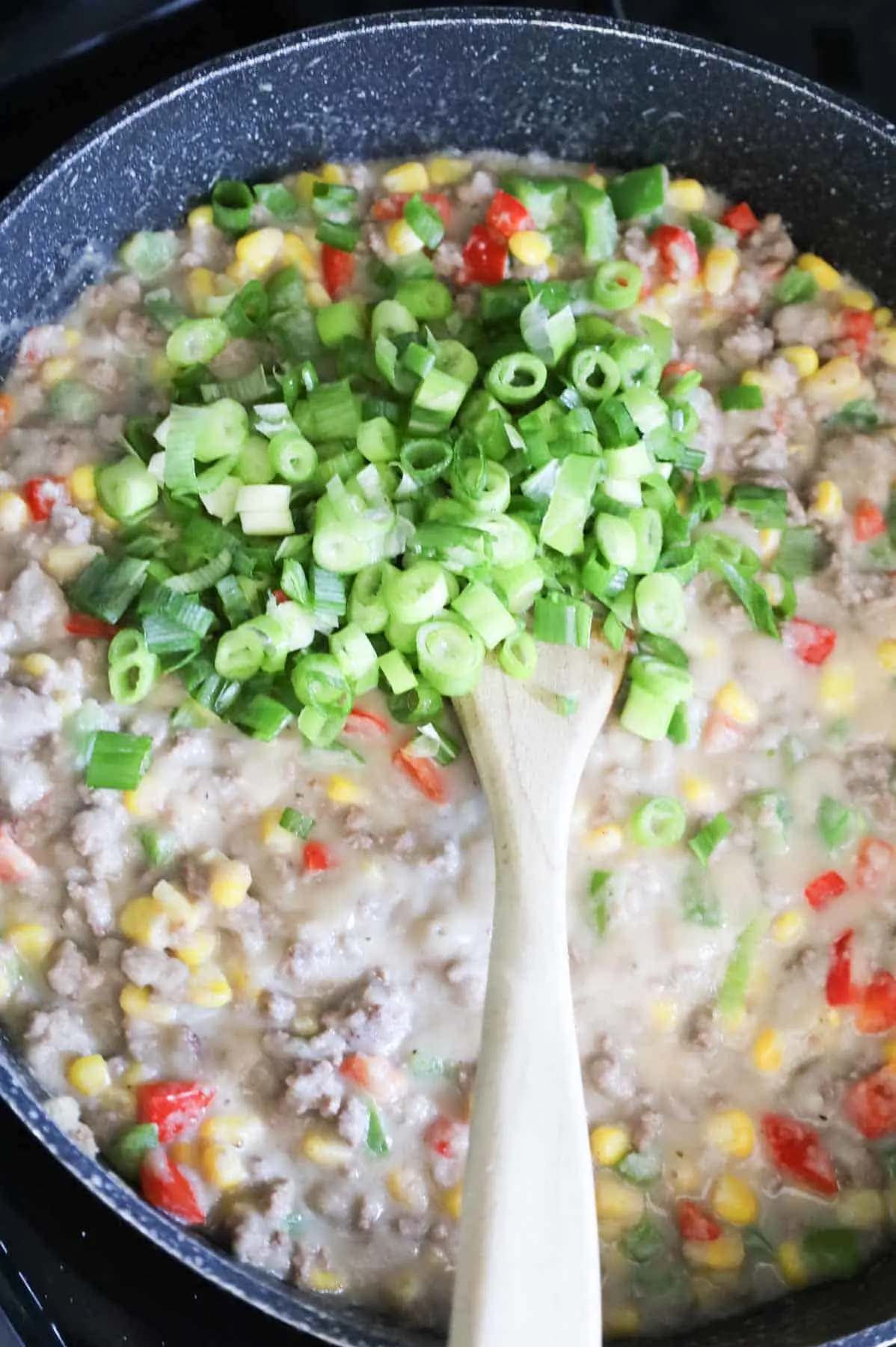 chopped green onions on top of mashed potato, ground beef and veggie mixture in a skillet