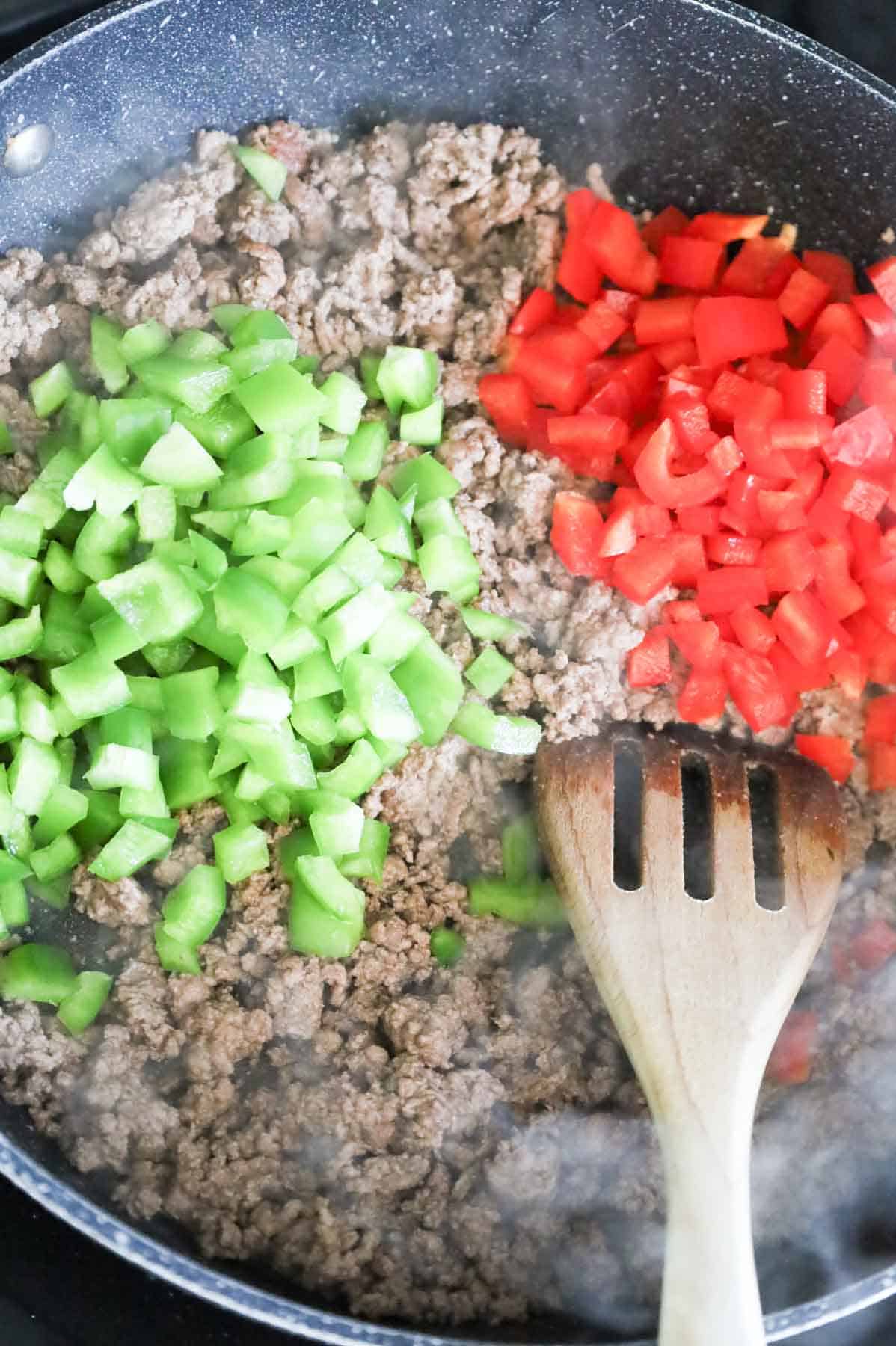 diced red and green bell peppers on top of browned ground beef in a skillet