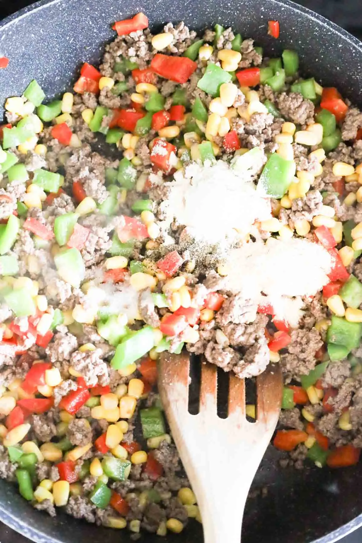 spices on top of ground beef, corn and bell pepper mixture in a skillet