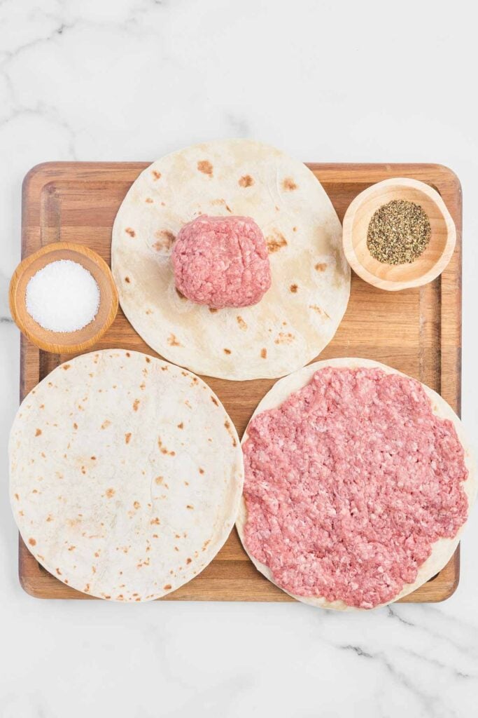 ground beef being flattened into patties on flour tortillas