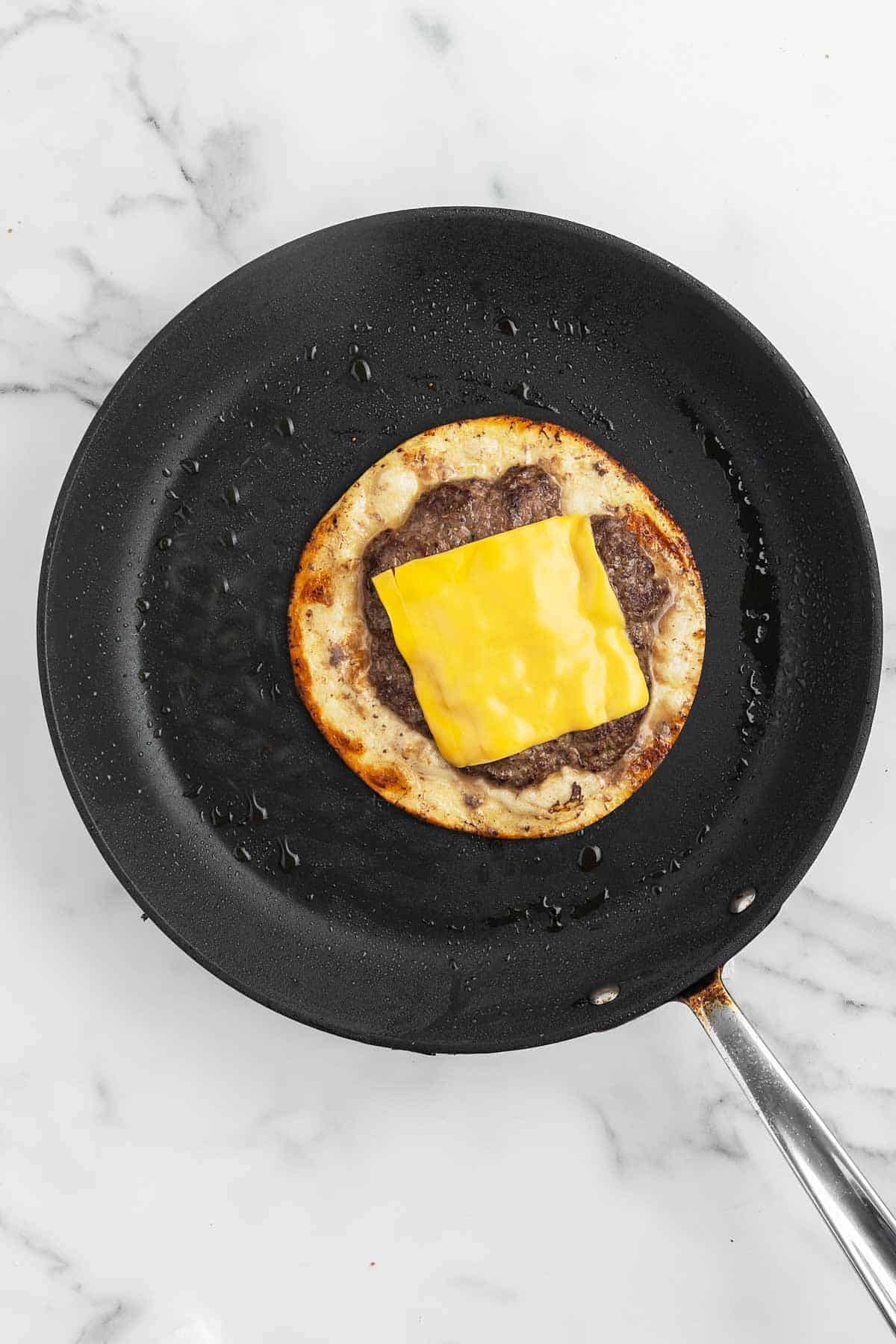 slice of cheese on top of smash burger taco in a skillet