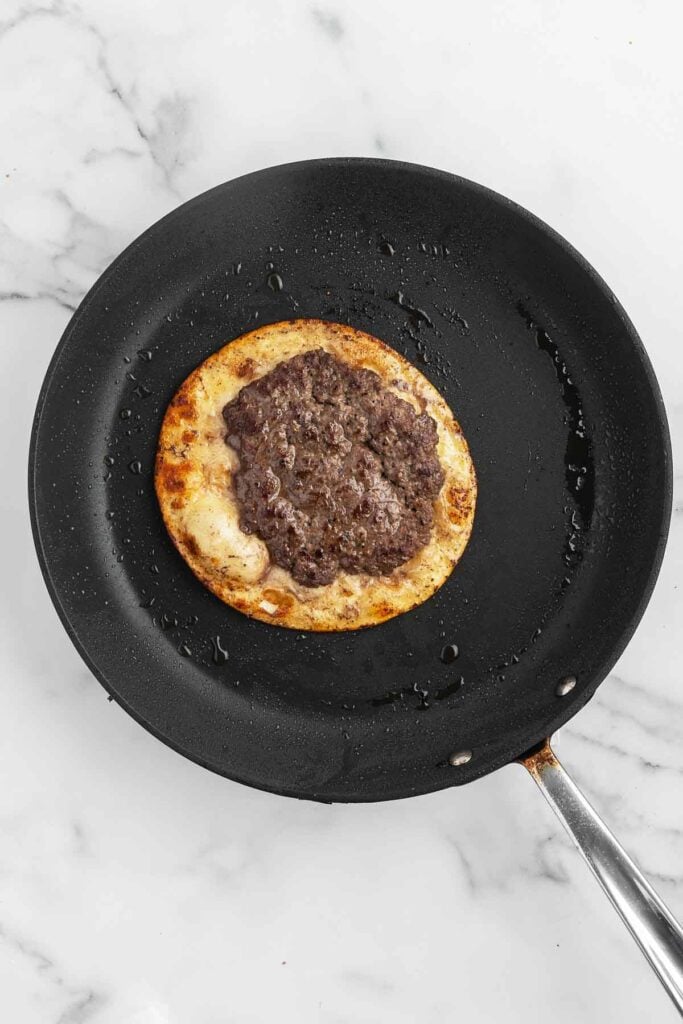 smash burger patty on a tortilla cooking in a skillet