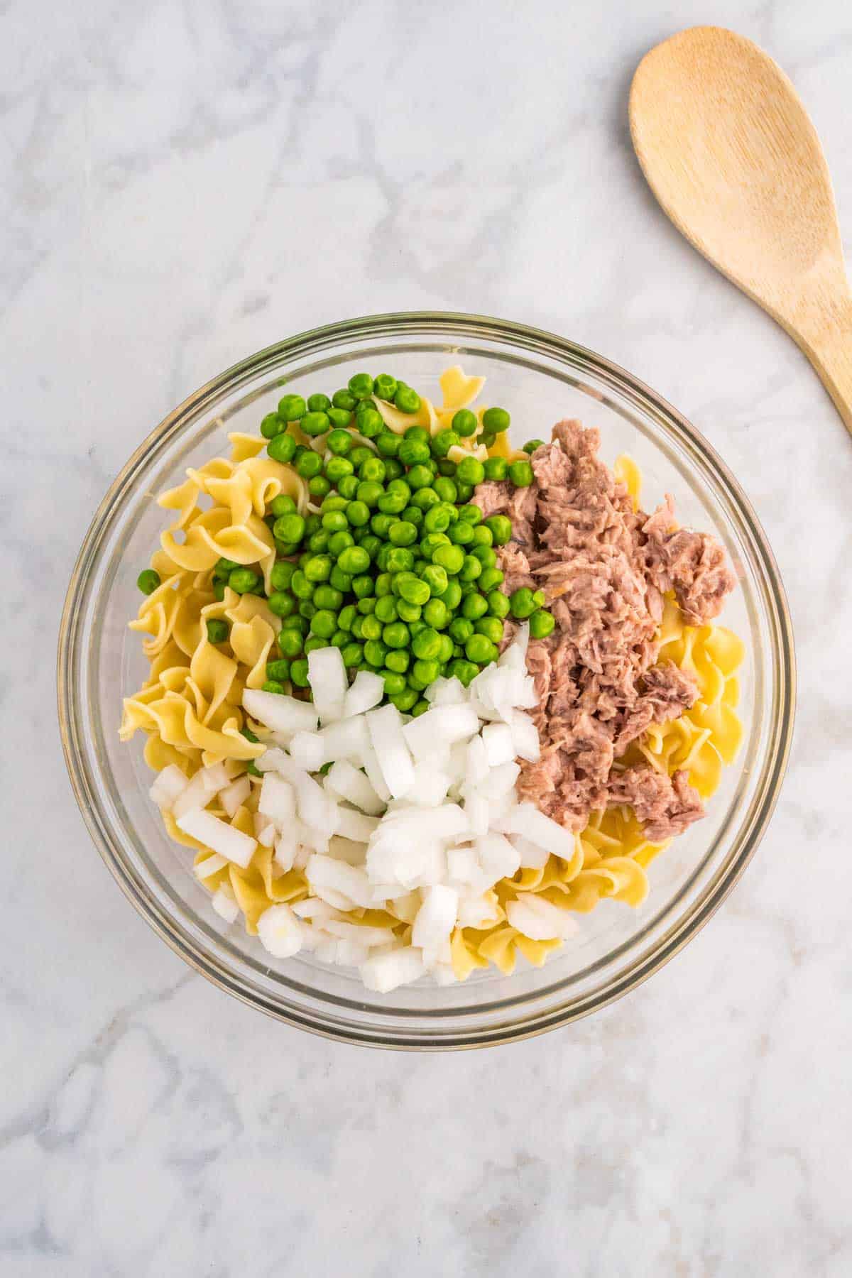 peas, flaked tuna, diced onions and cooked egg noodles in a mixing bowl