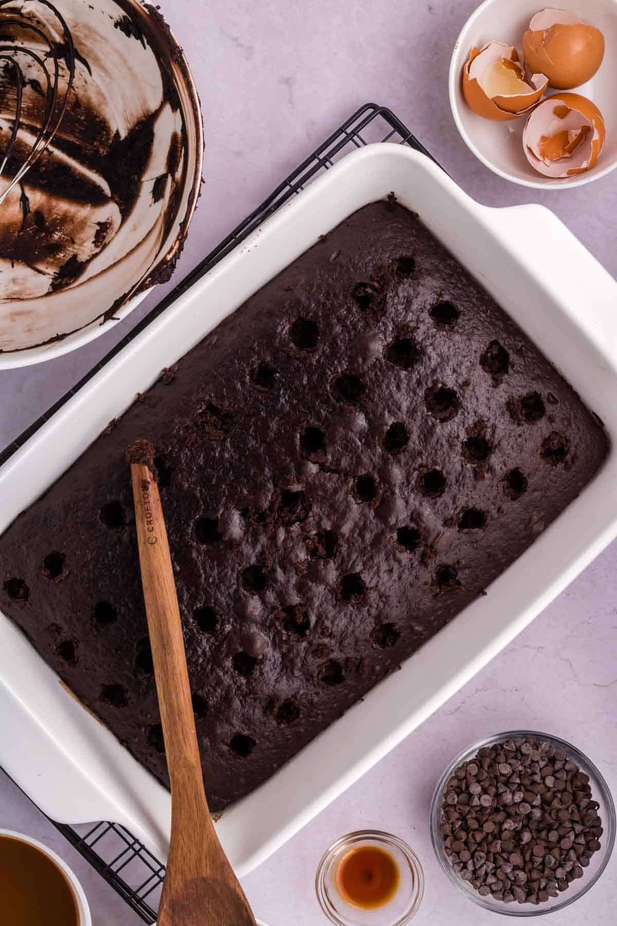 poking holes in a 9 x 13 inch chocolate cake with the handle of a wooden spoon