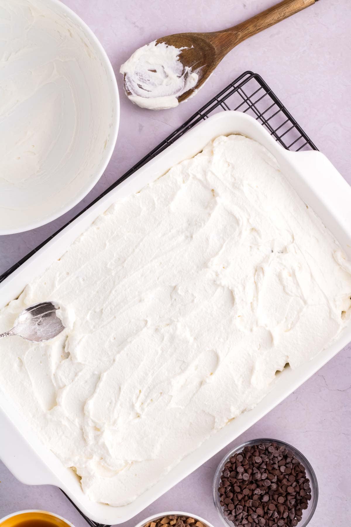 spreading whipped cream on top of a chocolate poke cake