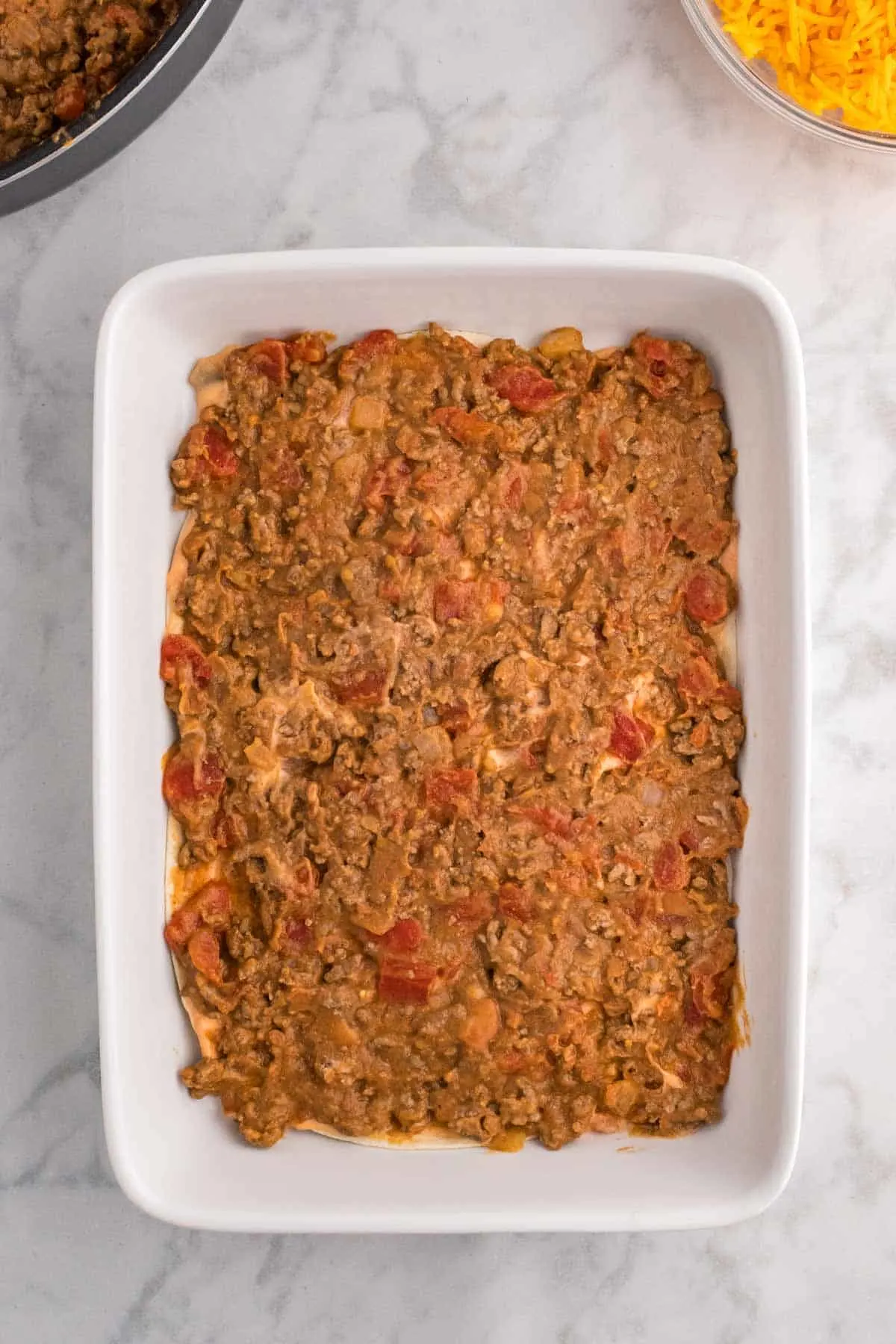 beef and refried bean mixture spread in a layer in a baking dish