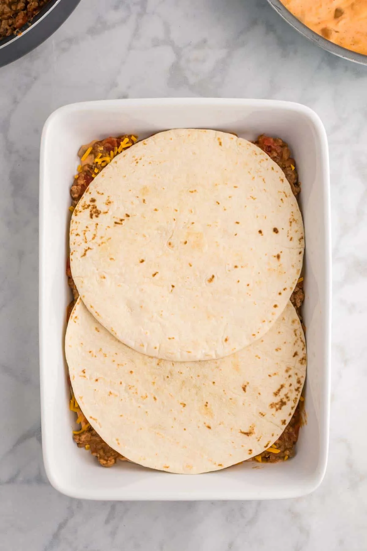 two flour tortillas on top of beef burrito mixture in a baking dish