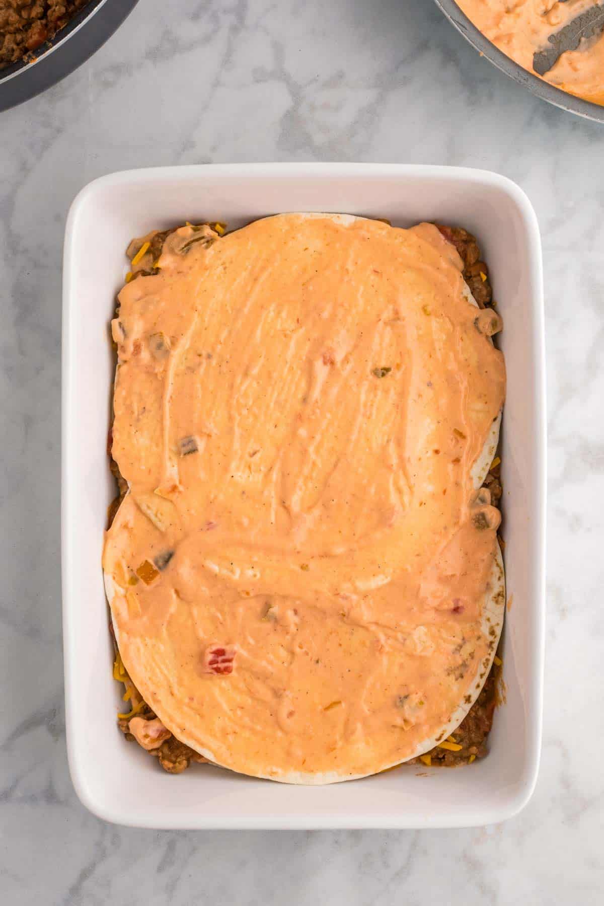 creamy salsa sauce mixture spread over tortillas in a baking dish