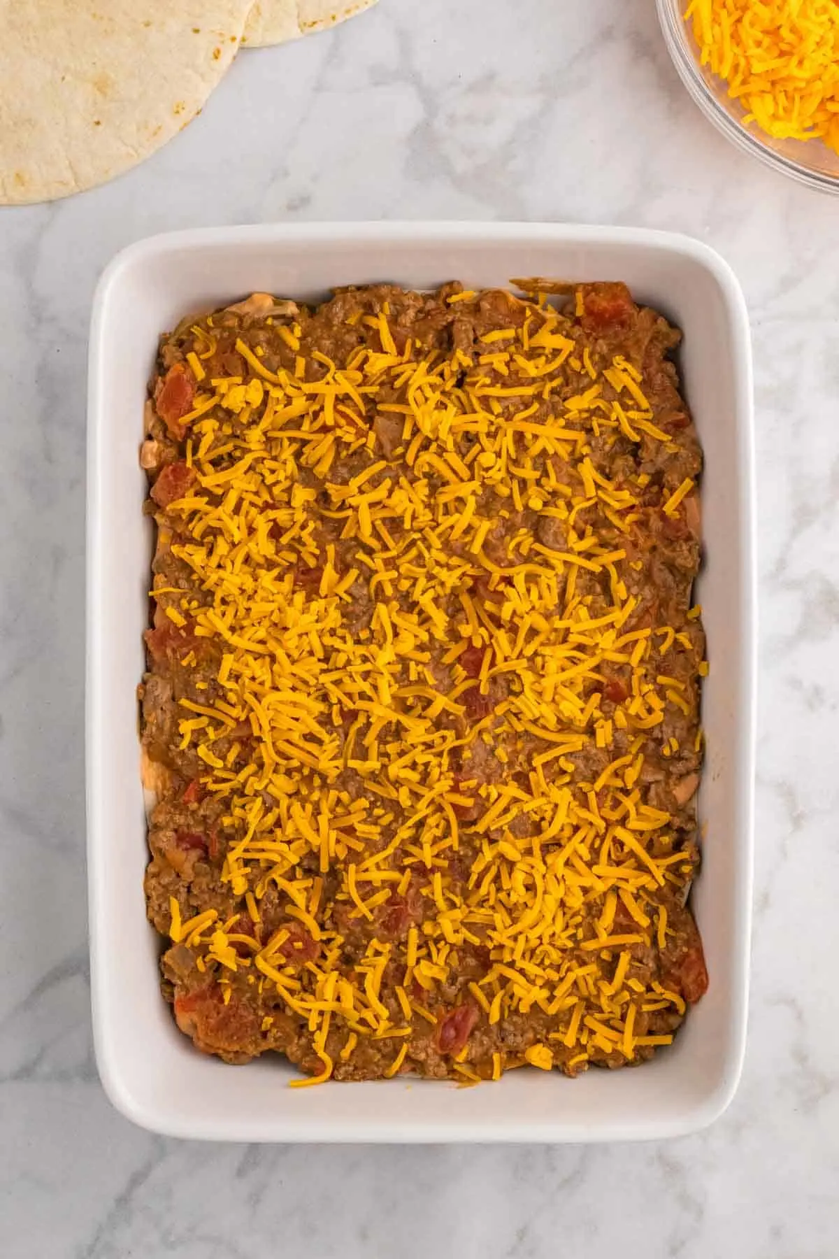 shredded cheddar cheese on top of beef burrito mixture in a baking dish