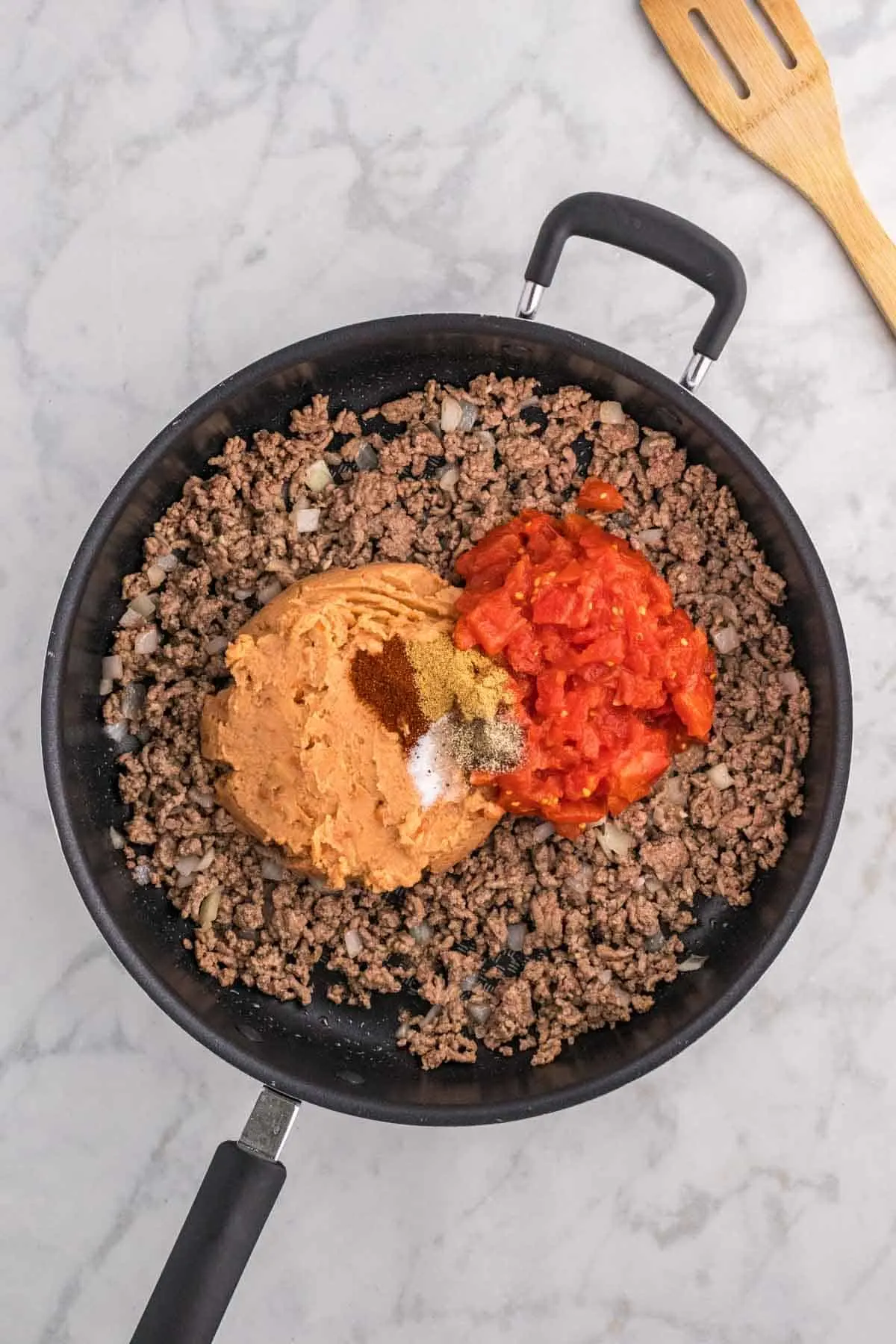 spices, refried beans and diced tomatoes on top of cooked ground beef in a skillet
