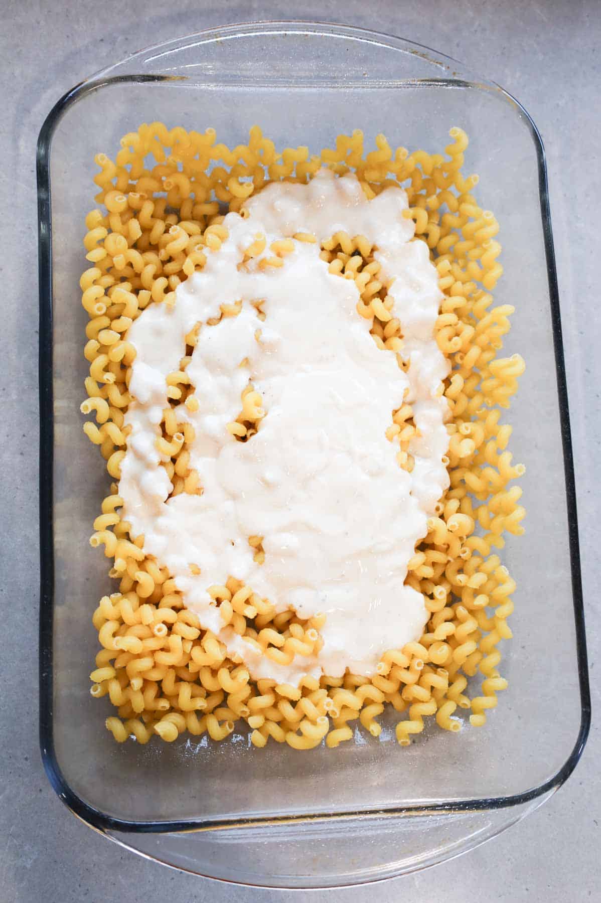 jarred alfredo sauce poured over uncooked noodles in a baking dish