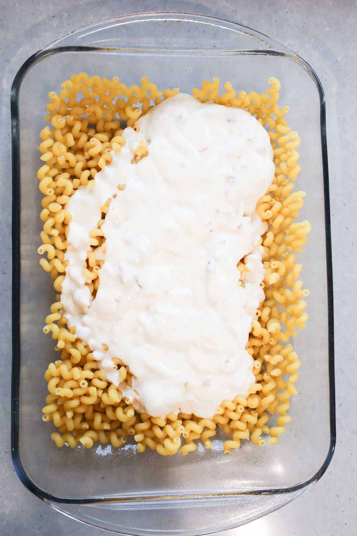 alfredo sauce and cream of bacon soup poured over pasta noodles in a baking dish