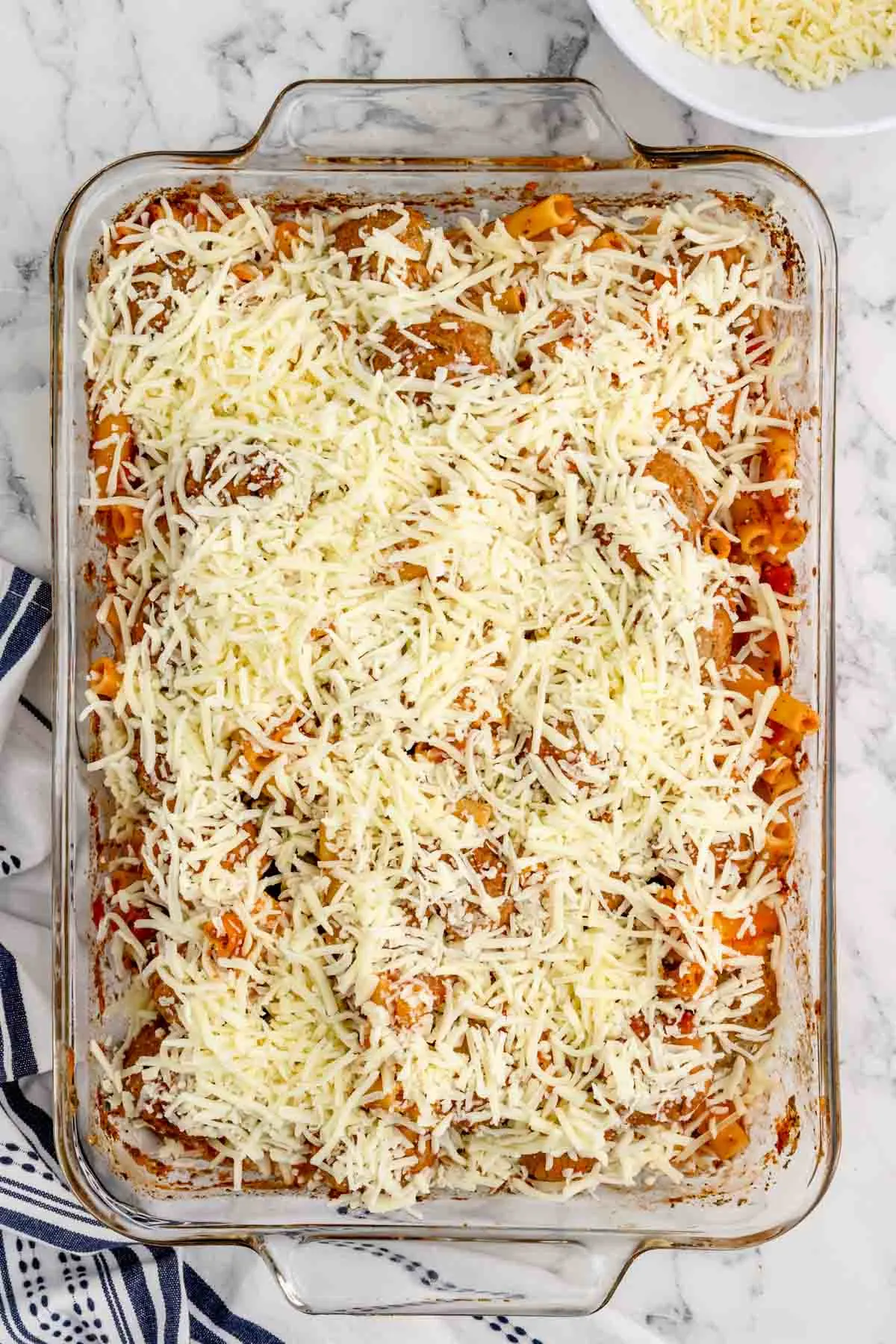 shredded mozzarella on top of meatballs and ziti in a baking dish