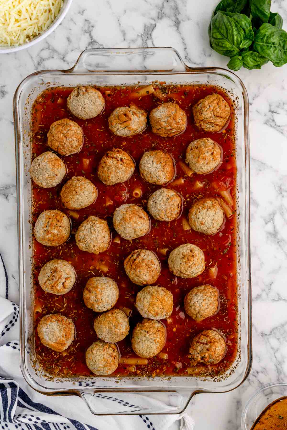 meatballs on top of uncooked ziti and sauce mixture in a baking dish