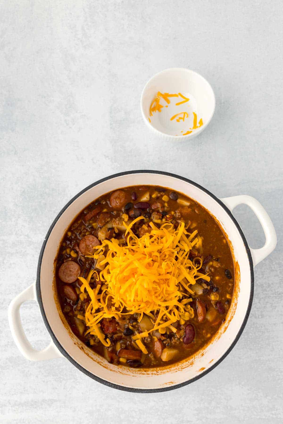 shredded cheddar cheese added to cowboy stew in a Dutch oven