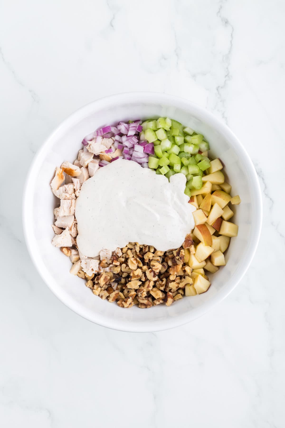 dressing poured on top of chicken salad ingredients in a mixing bowl