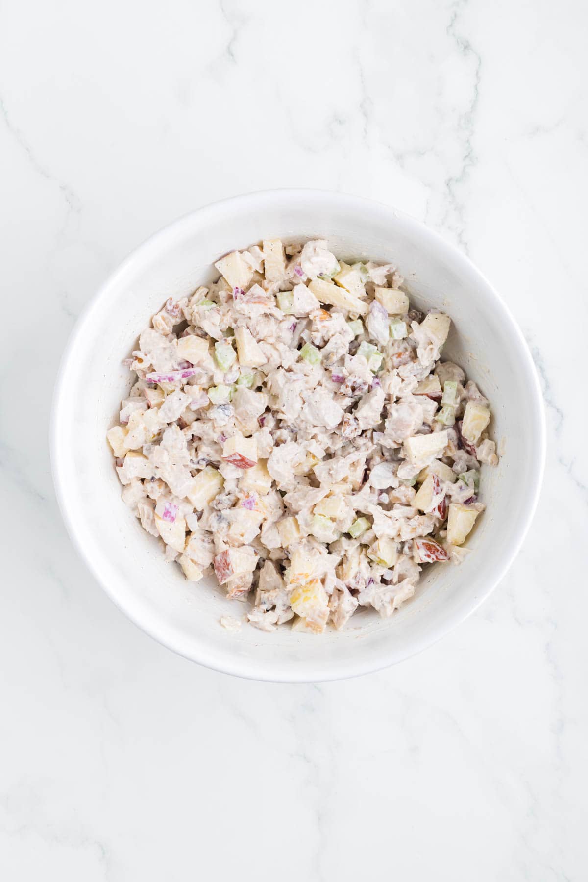 chicken salad ingredients and dressing stirred together in a mixing bowl