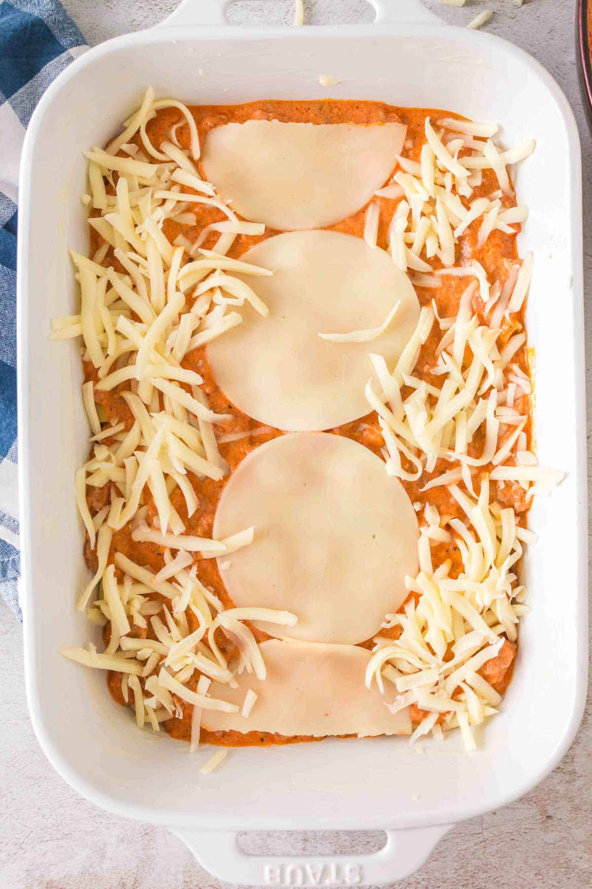 provolone cheese slices and shredded mozzarella cheese on top of ziti and sauce in a baking dish