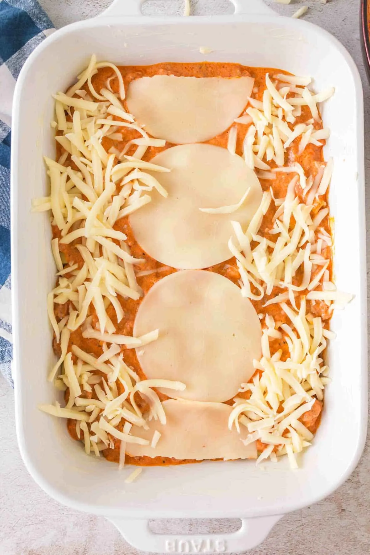 provolone cheese slices and shredded mozzarella cheese on top of ziti and sauce in a baking dish