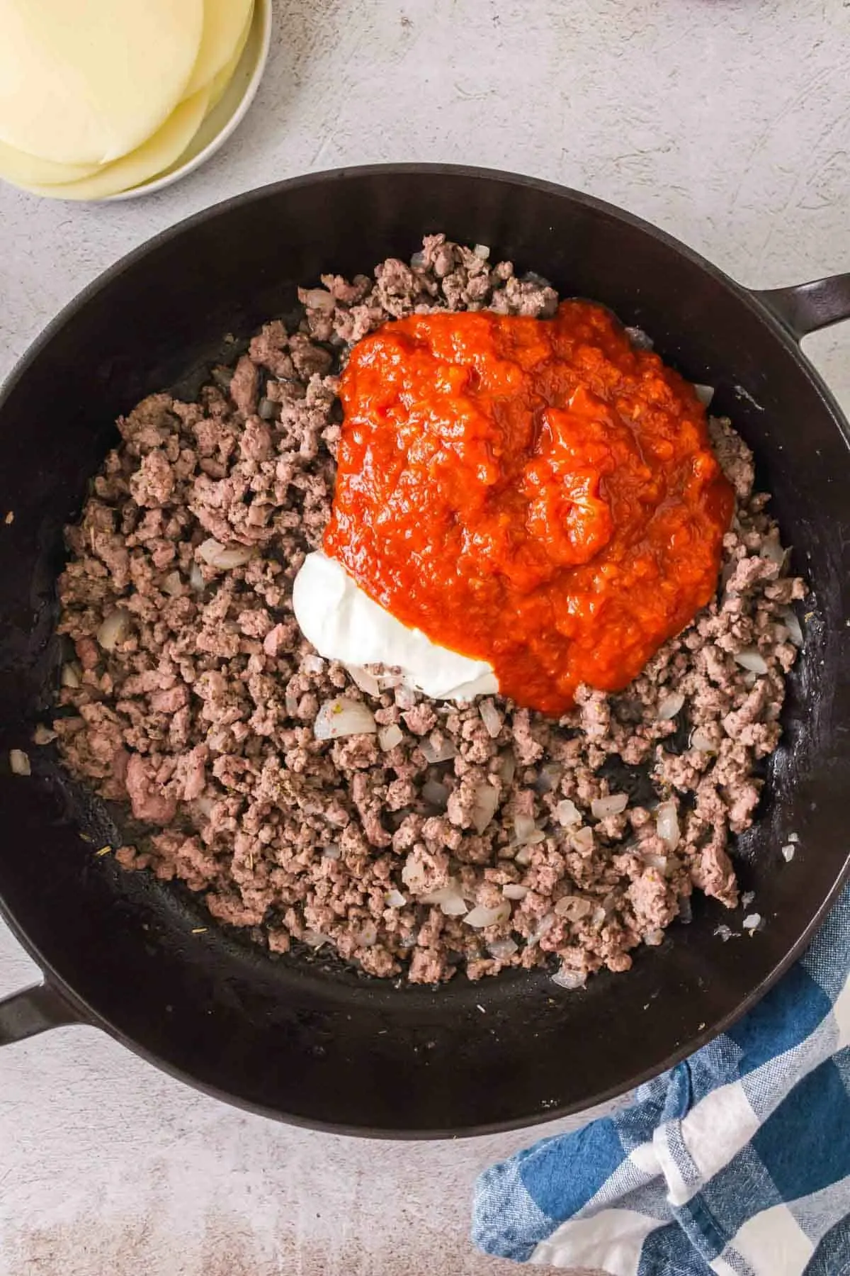 marinara sauce and sour cream on top of cooked ground beef in a skillet