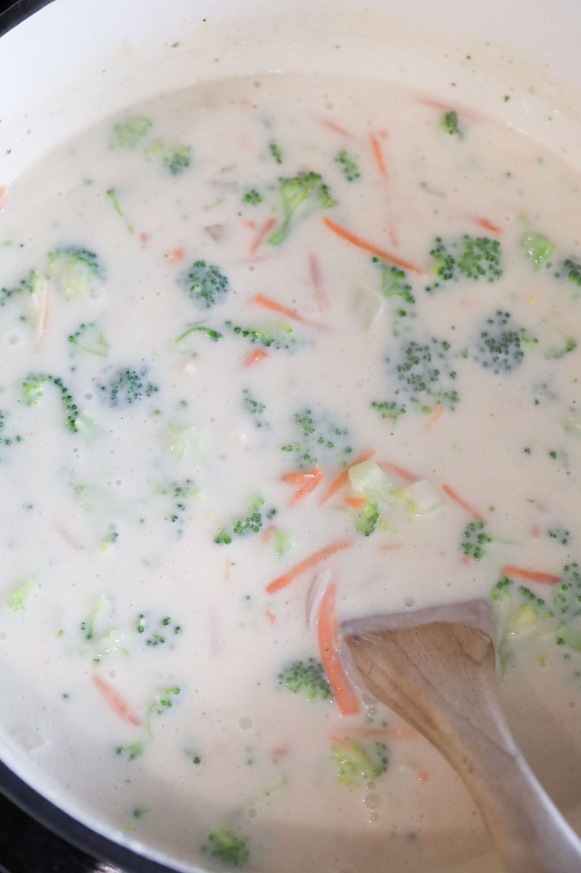 broccoli florets and shredded carrots being stirred into creamy soup