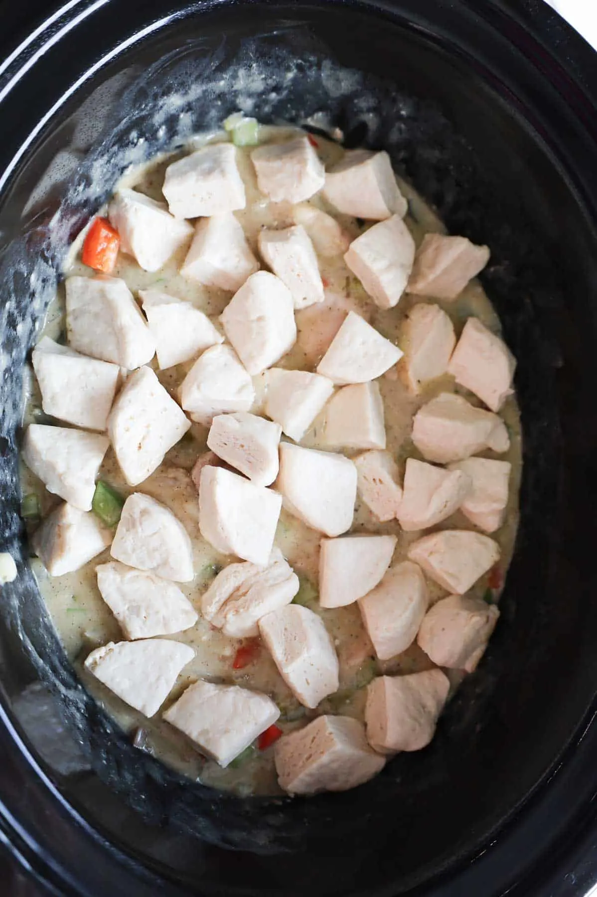 raw Pillsbury biscuit pieces sprinkled on top of creamy chicken mixture in a Crock Pot