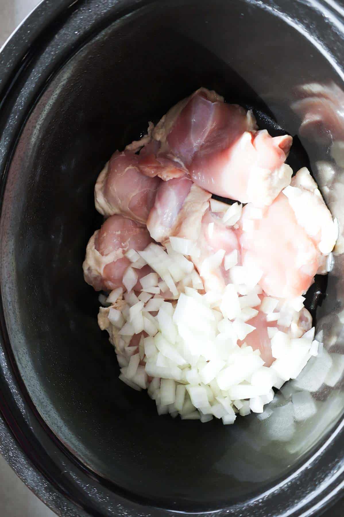 diced onions on top of chicken thighs in a Crock Pot