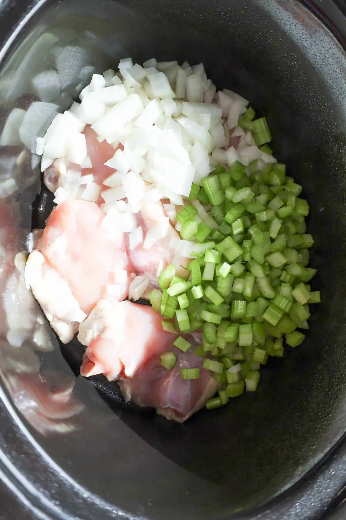 diced onions and celery on top of raw chicken thighs in a Crock Pot