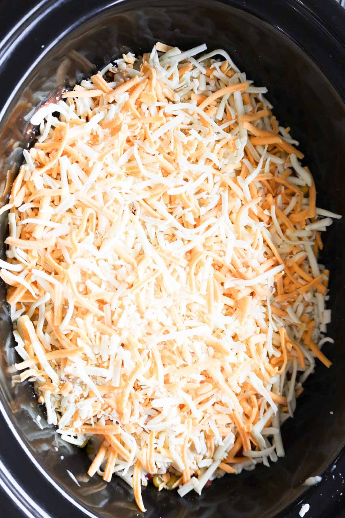 shredded cheddar cheese on top of tater tot casserole in a crock pot