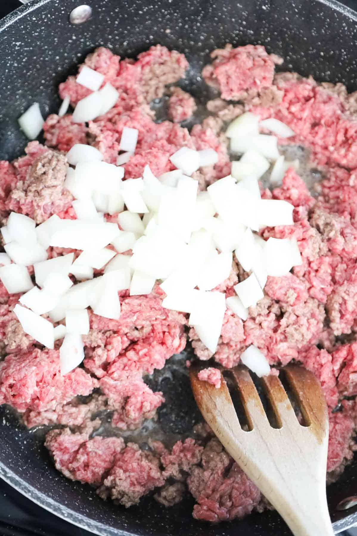 diced onions on top of ground beef in a skillet