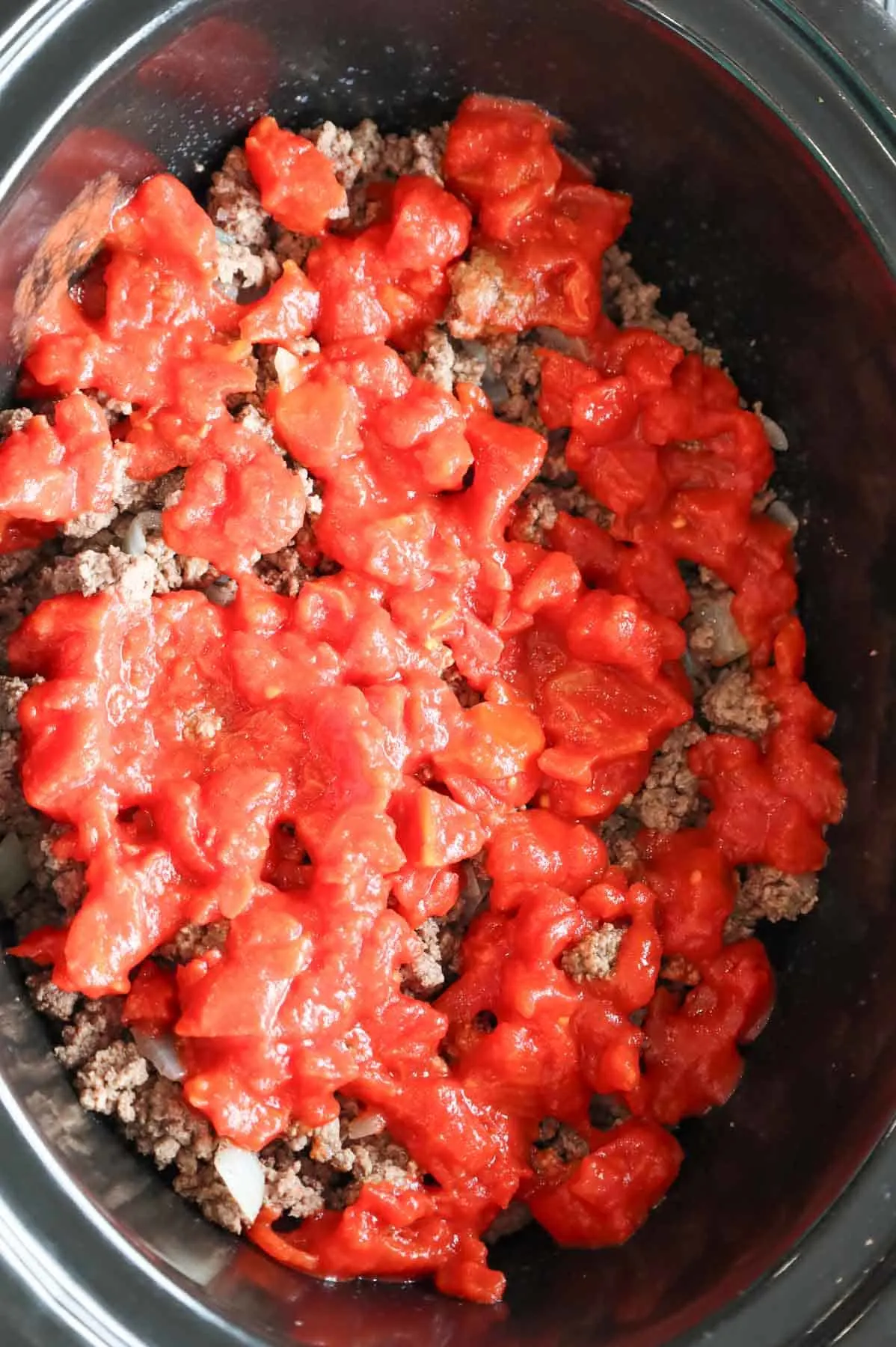 diced tomatoes on top of cooked ground beef in a slow cooker