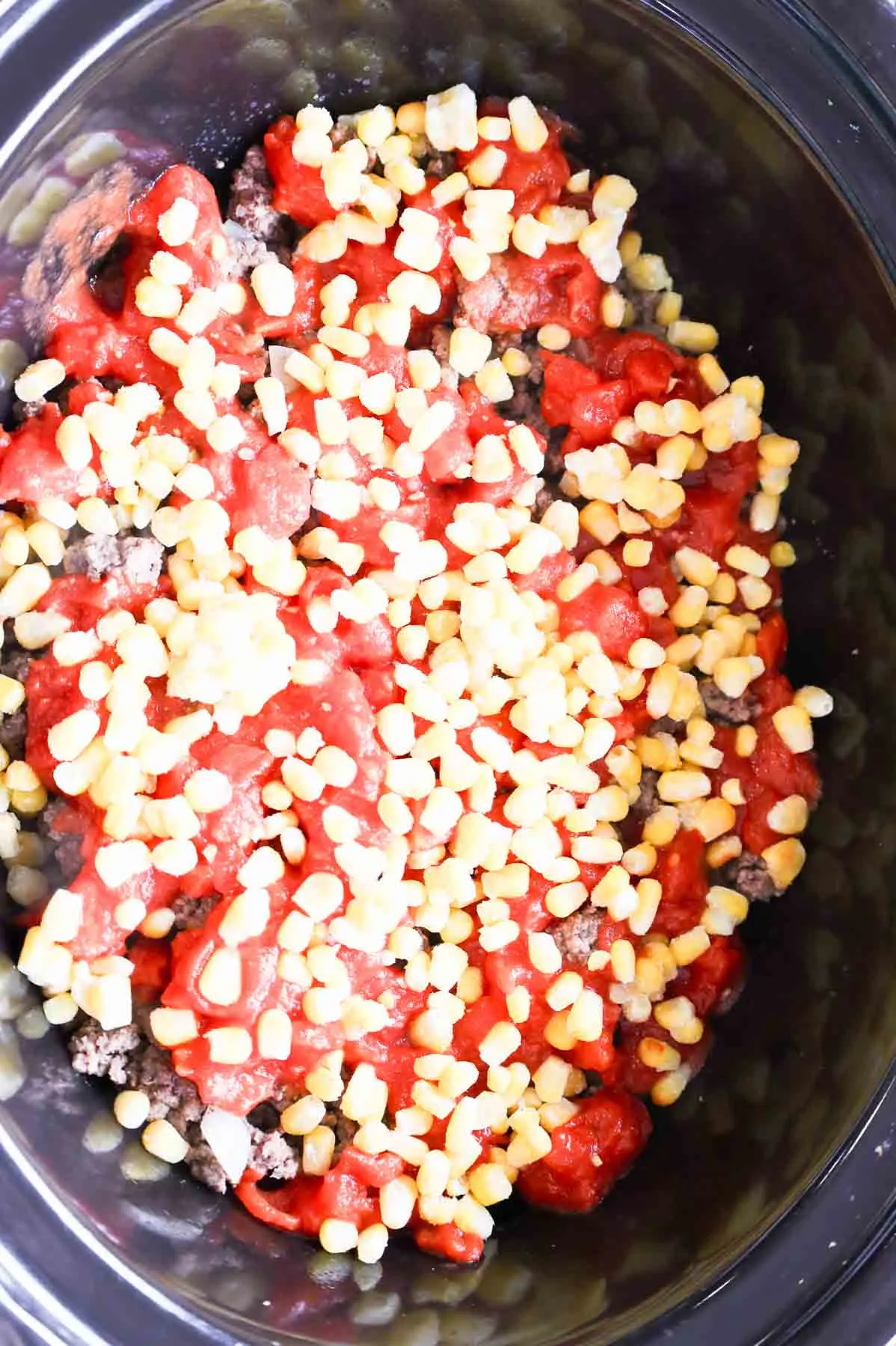 frozen corn and diced tomatoes on top of cooked ground beef in a slow cooker