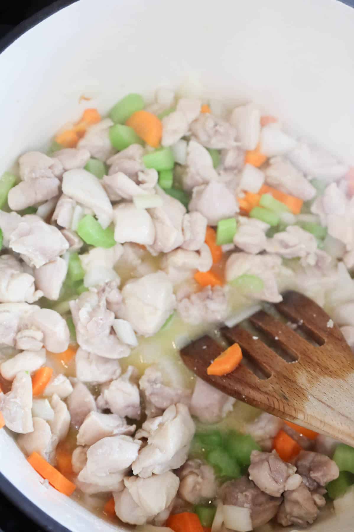 chicken pieces and chopped veggies cooking in butter in a pot