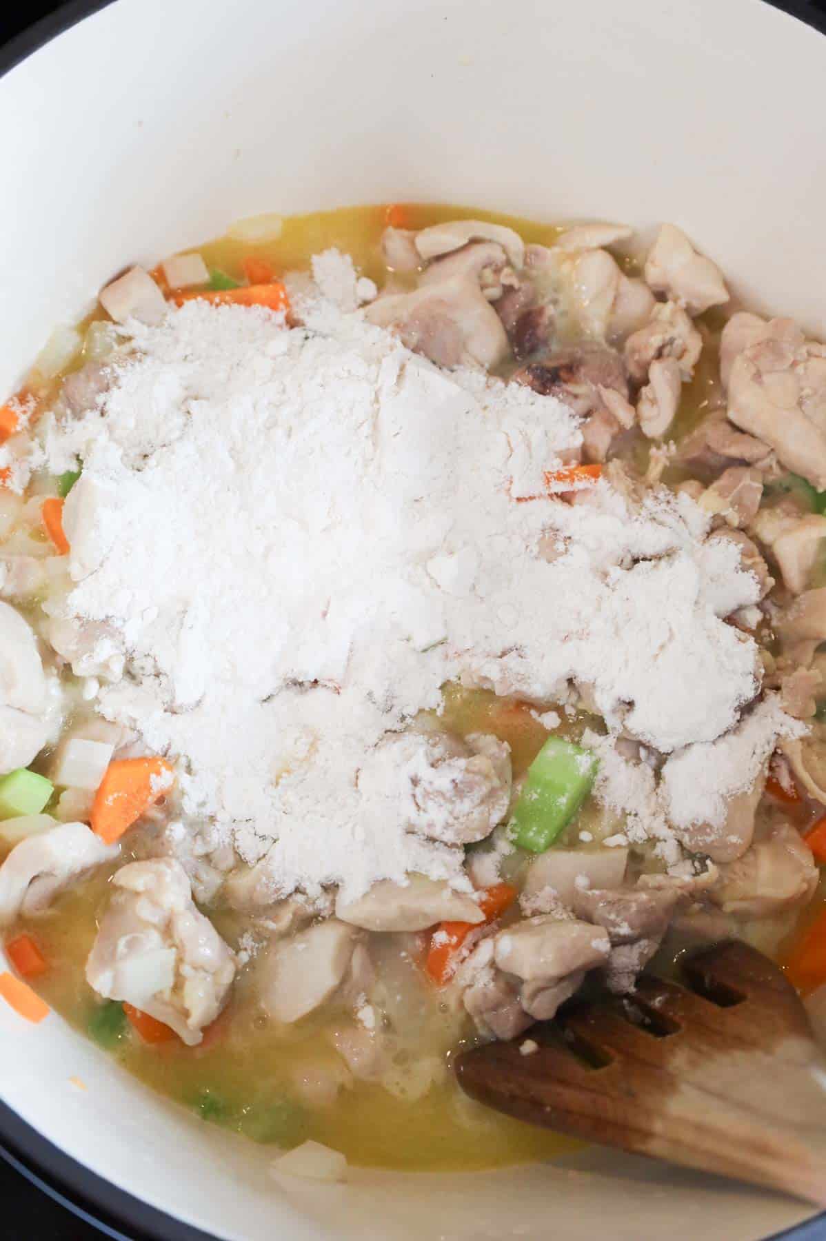 flour on top of butter, chicken and veggie mixture in a pot