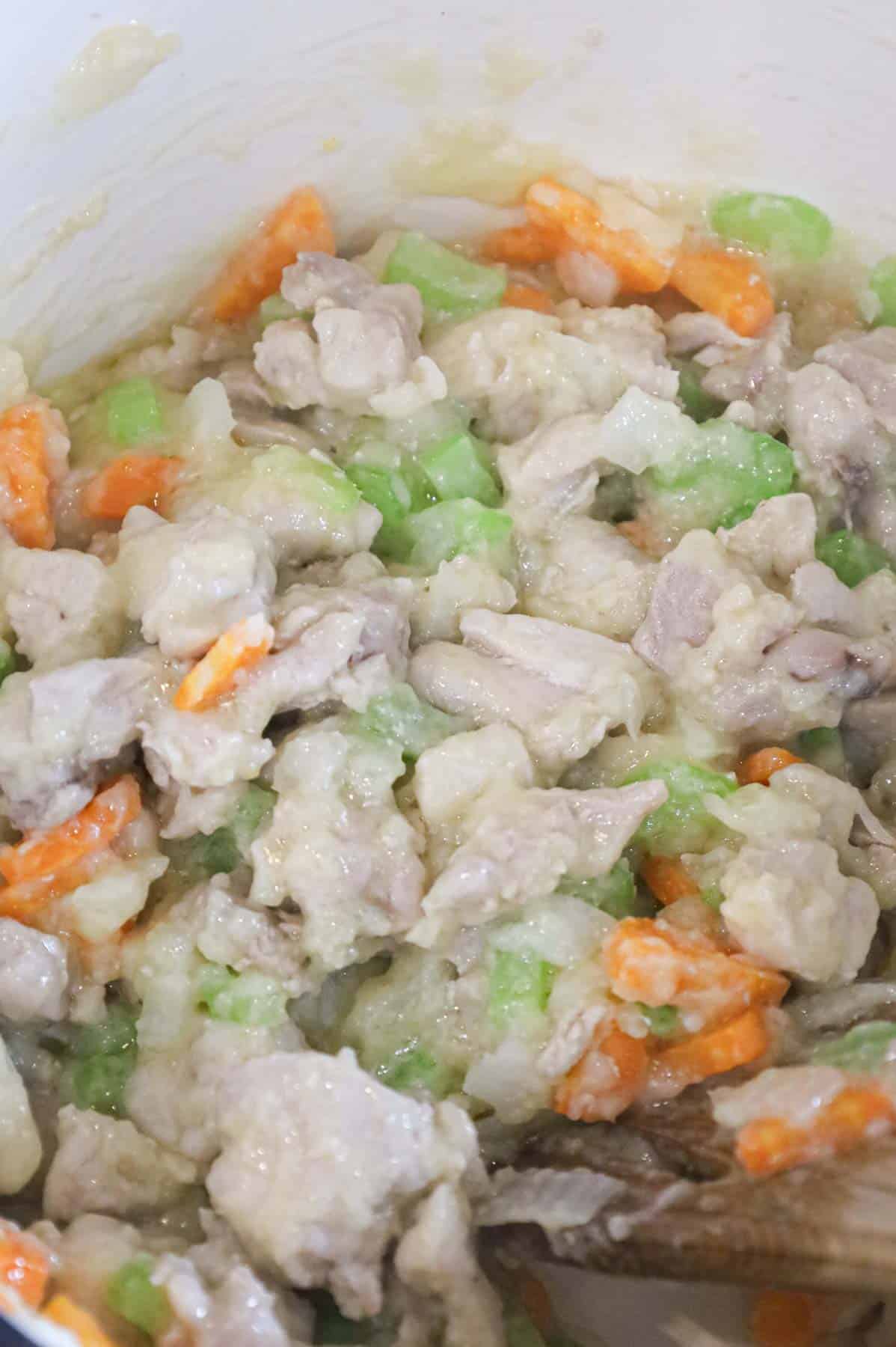 flour and butter paste coating pieces of chicken and veggies in a pot