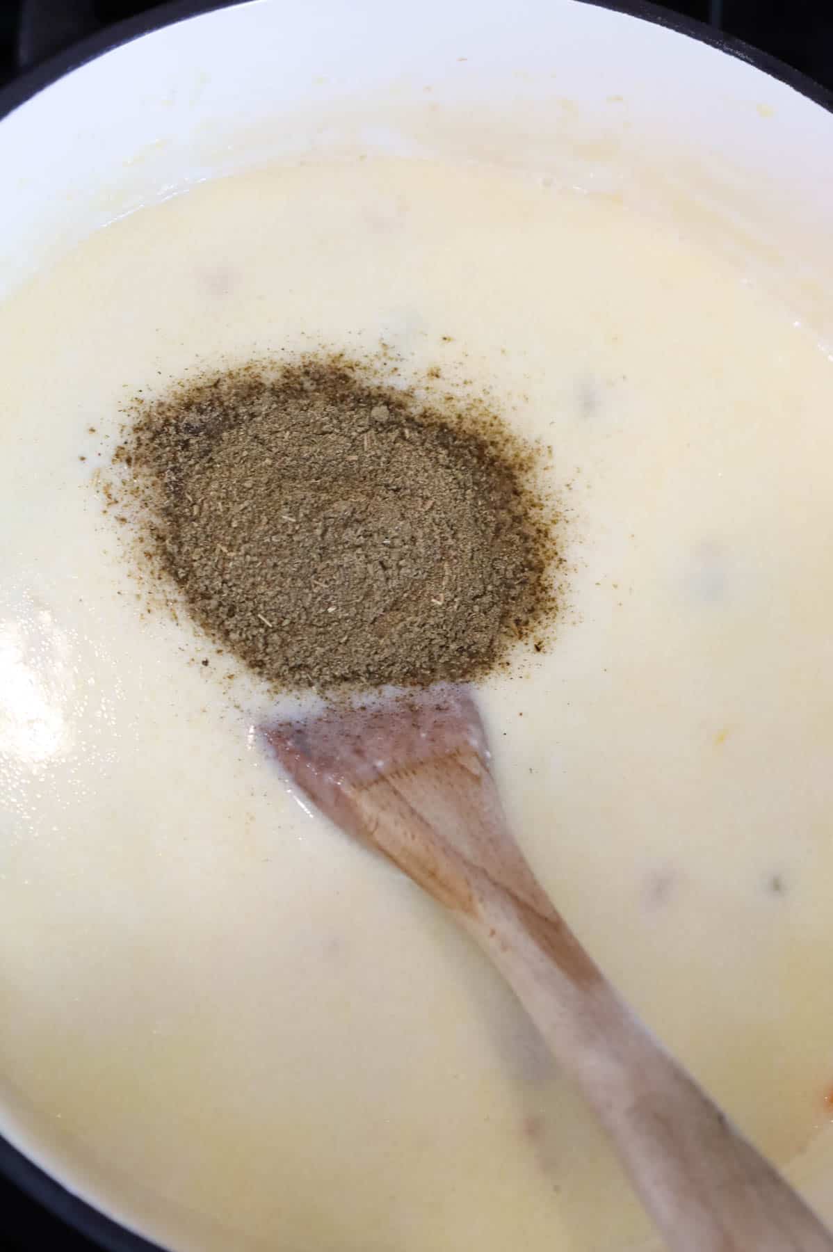 poultry seasoning added to creamy chicken soup in a pot
