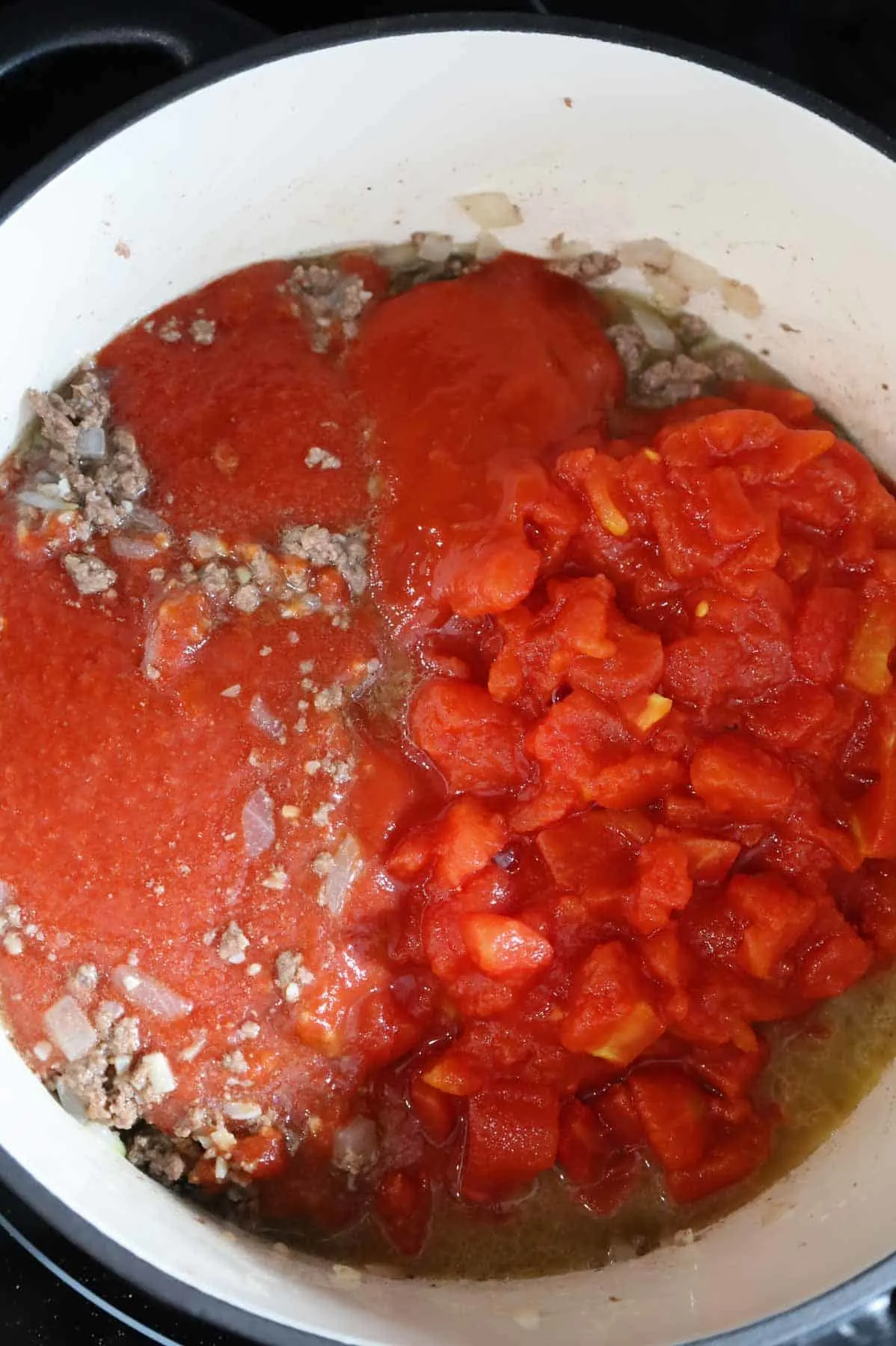 tomato sauce and diced tomatoes on top of cooked ground beef in a pot