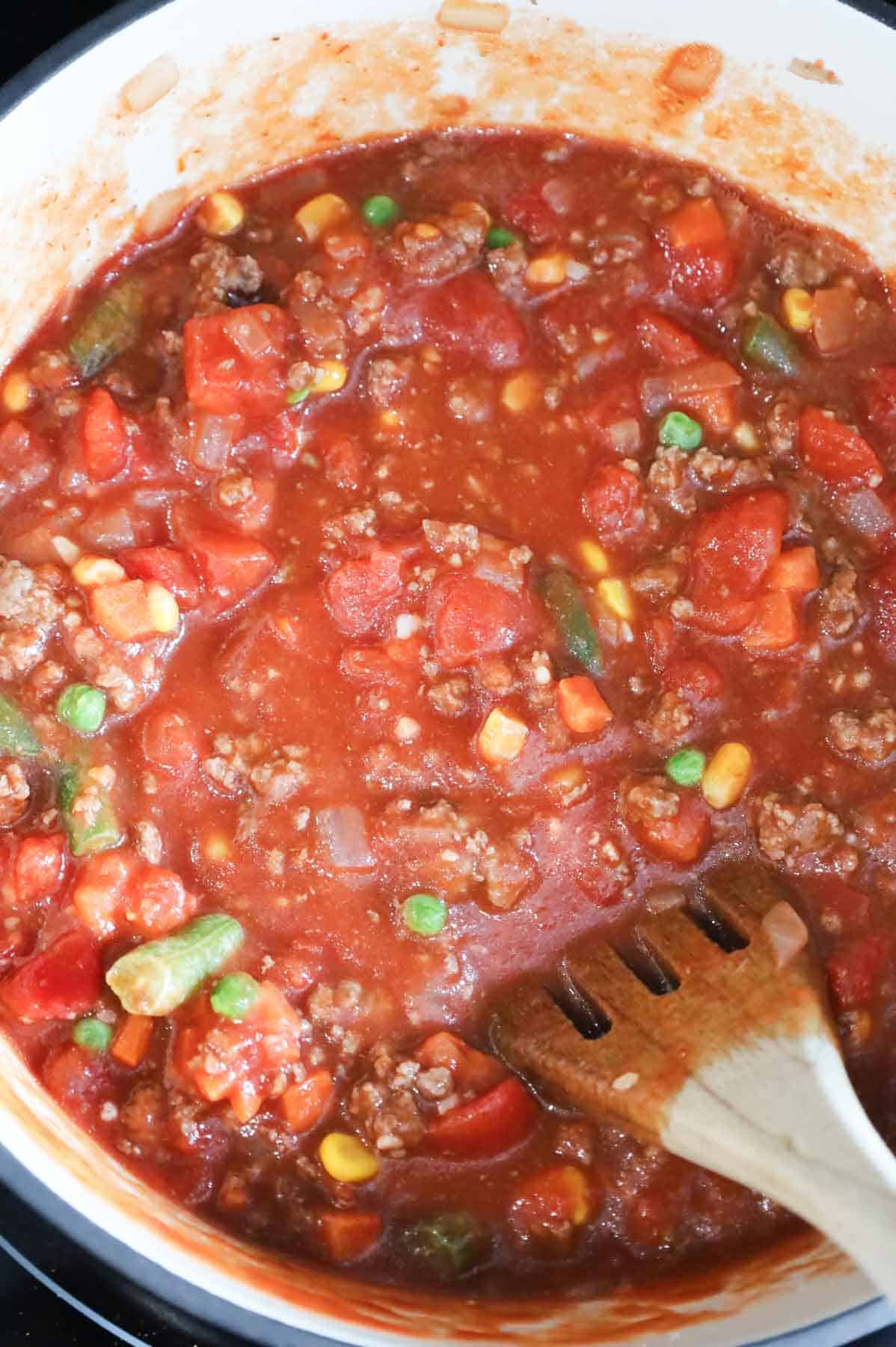 diced tomatoes, tomato sauce, mixed veggies and ground beef being stirred together in a pot