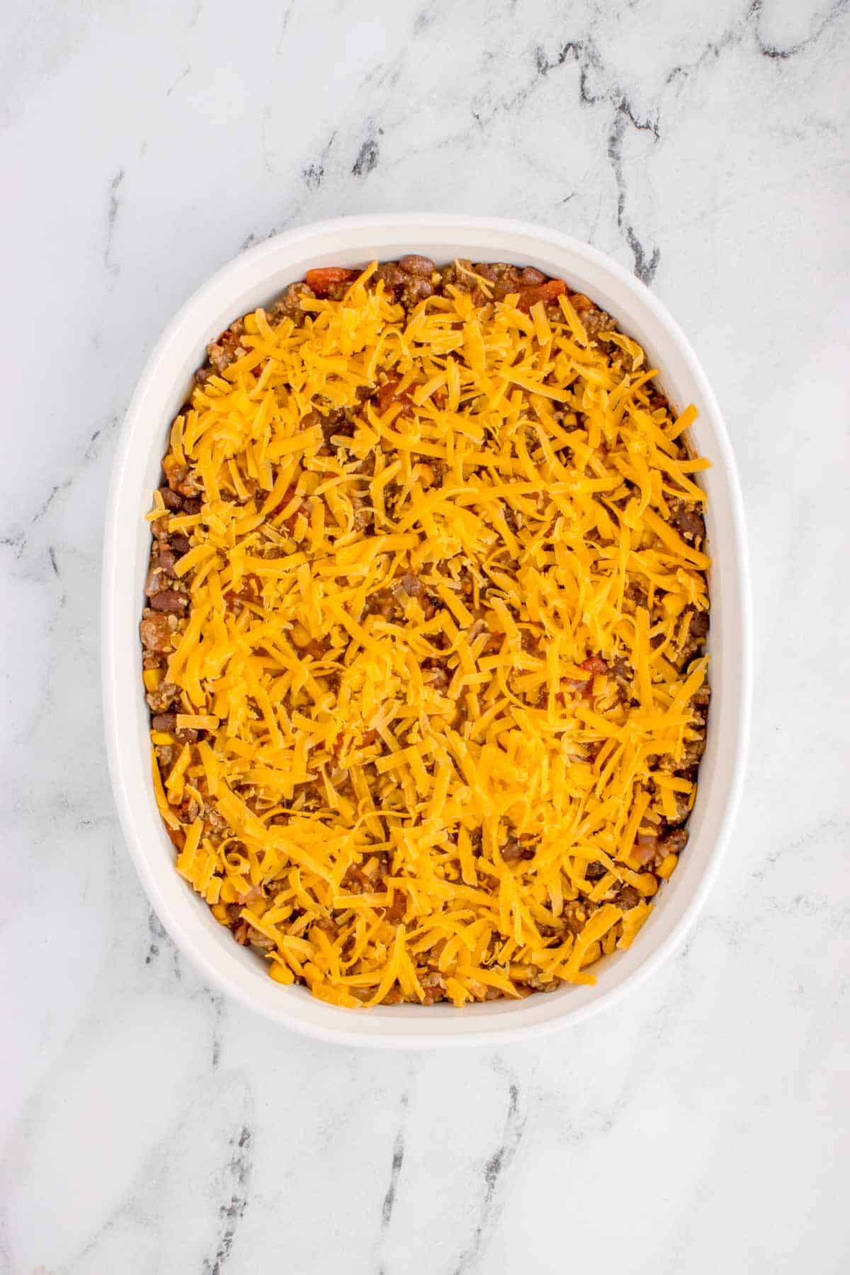 shredded cheddar cheese on top of ground beef mixture in a baking dish