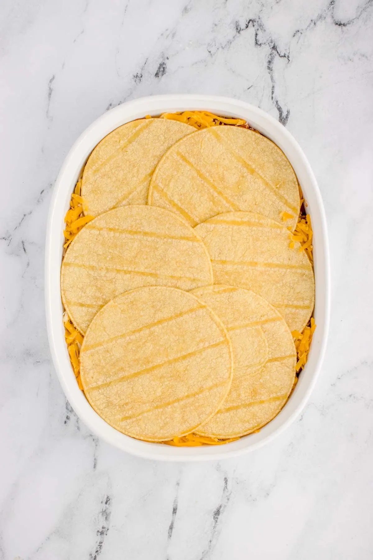 corn tortillas on top of shredded cheese layer in a baking dish