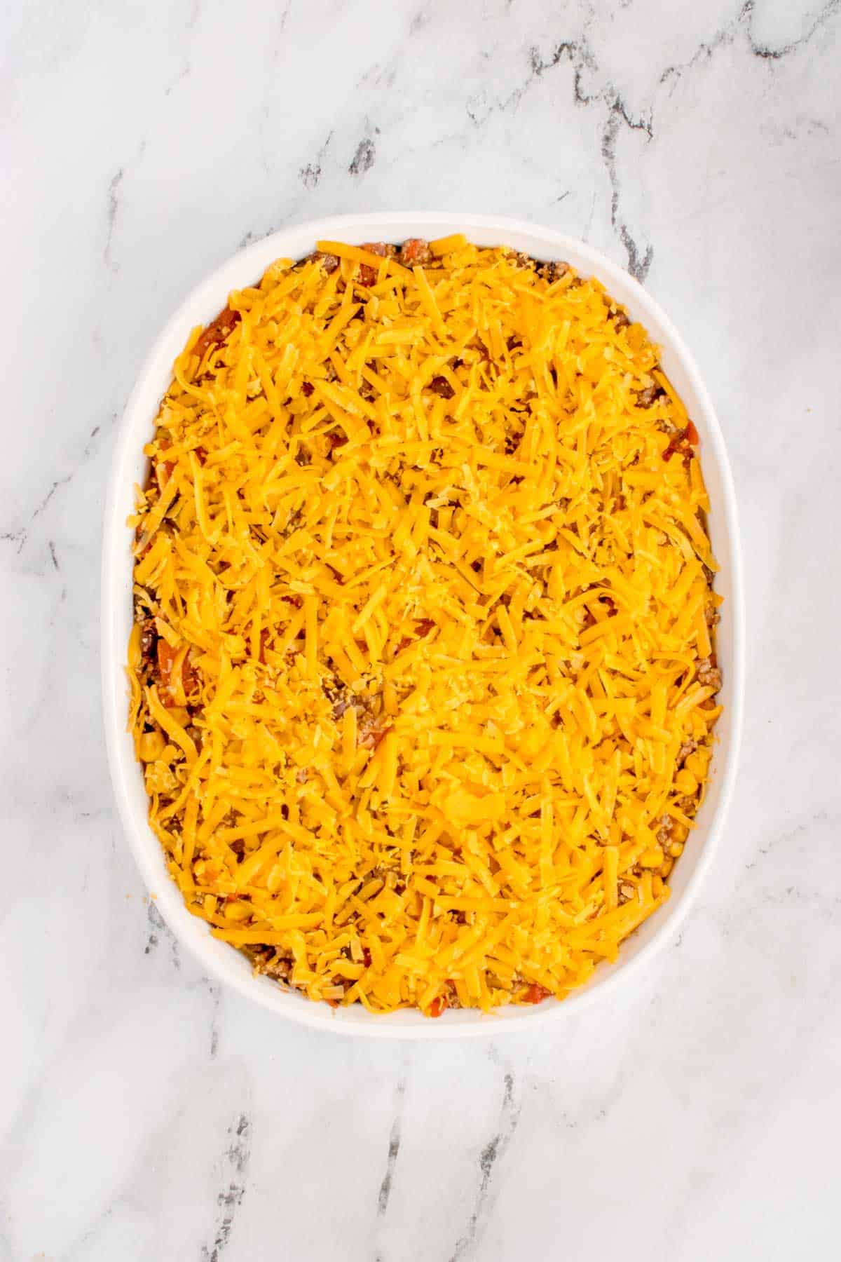 shredded cheese on top of ground beef casserole in a baking dish