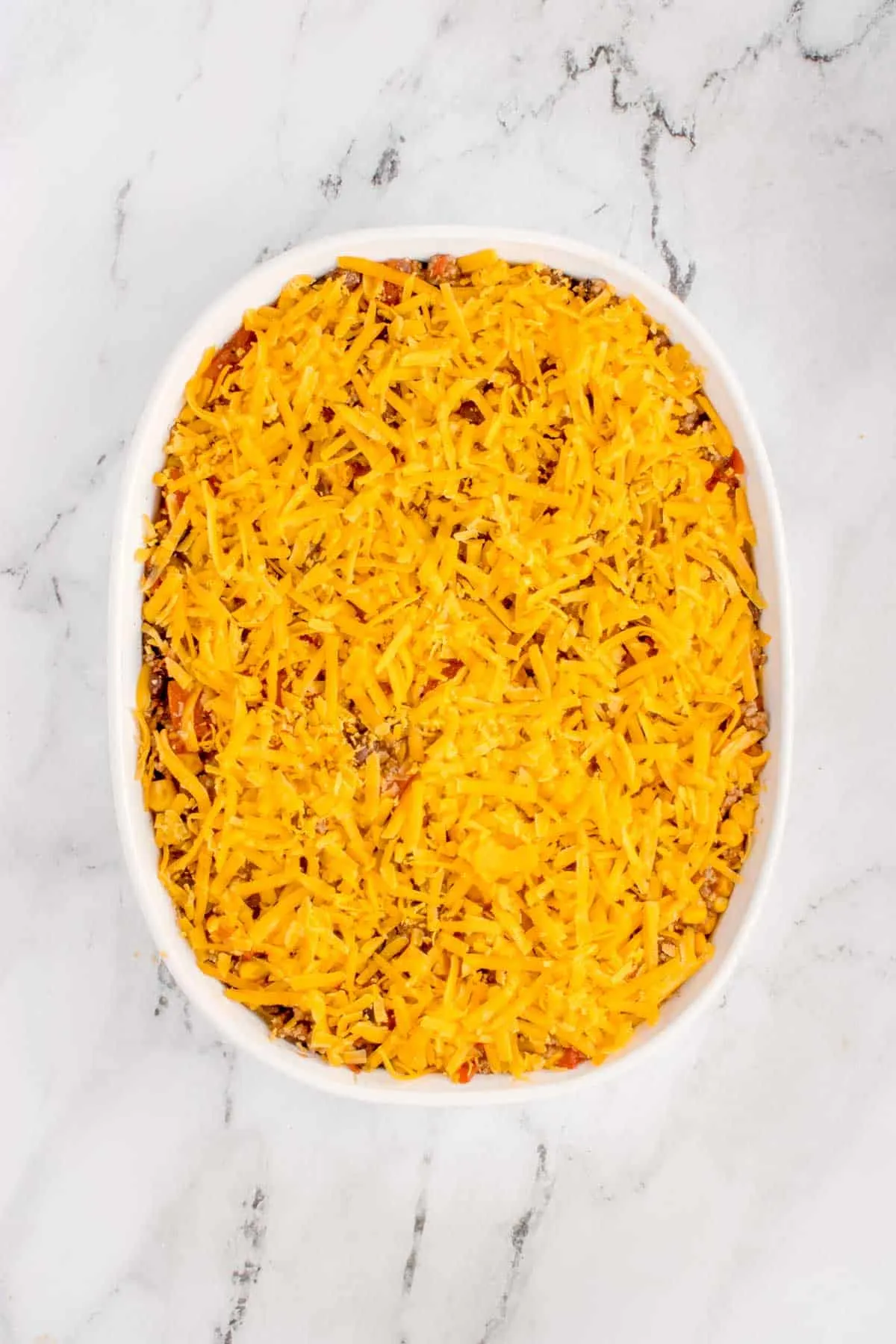 shredded cheese on top of ground beef casserole in a baking dish
