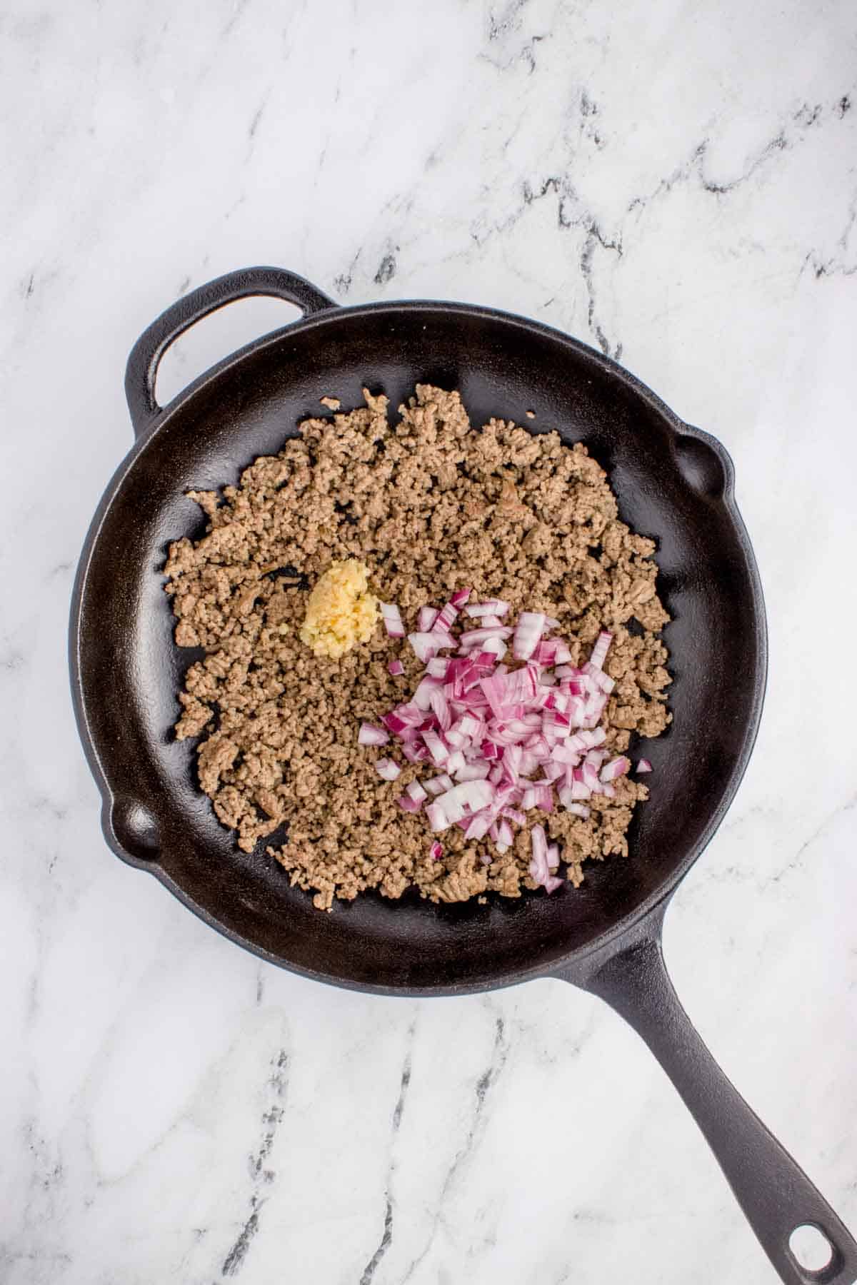 minced garlic and diced onions on top of cooked ground beef in a skillet