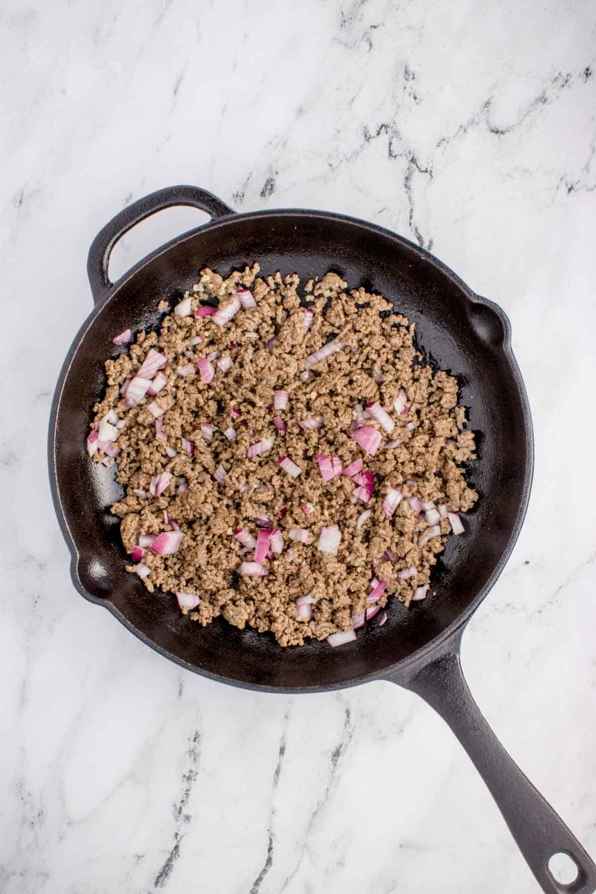 ground beef and diced onions cooking in a skillet